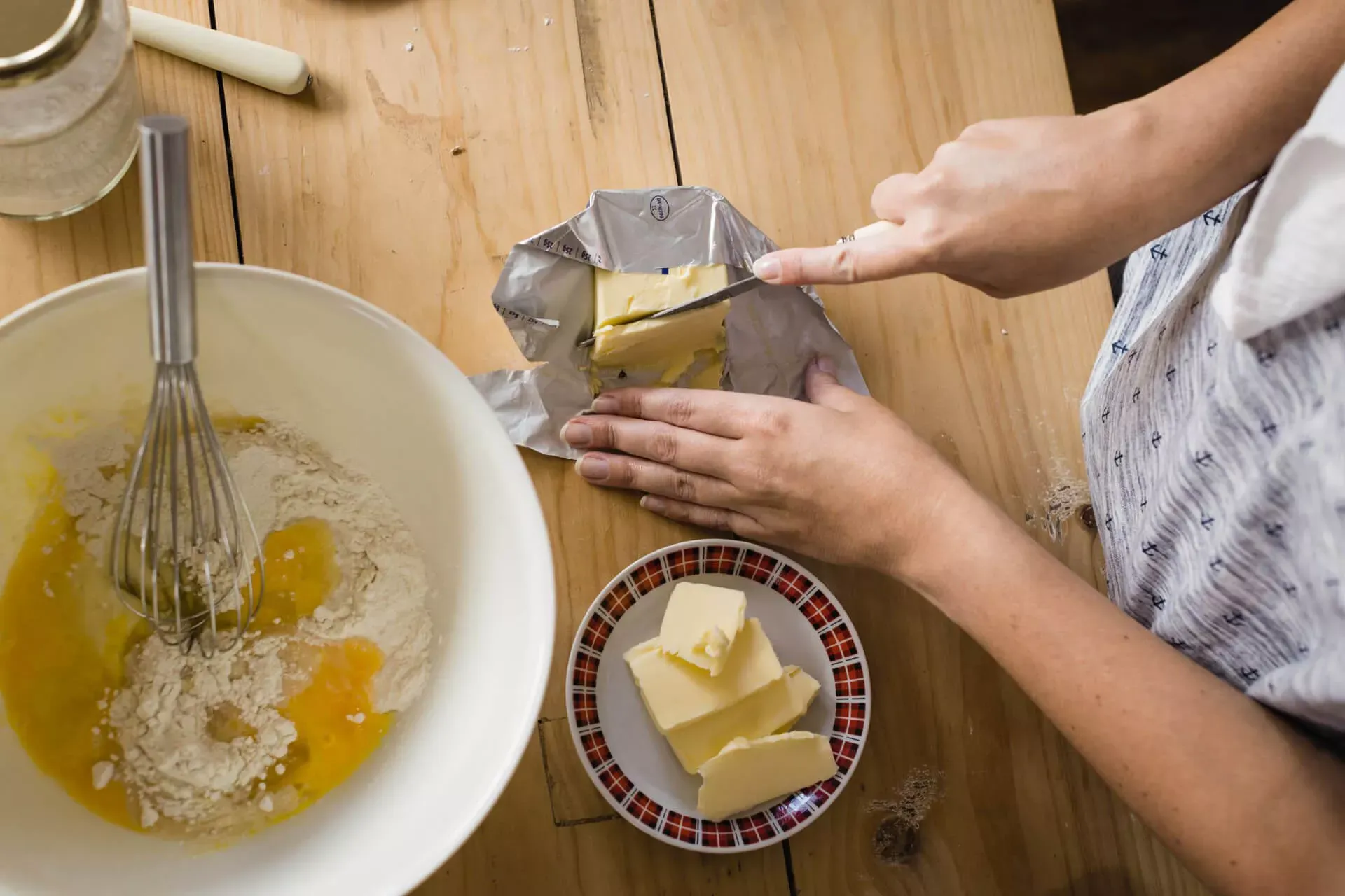 Frau schneidet ein Stück Butter ab, daneben eine Rührschüssel mit weiteren Backzutaten.