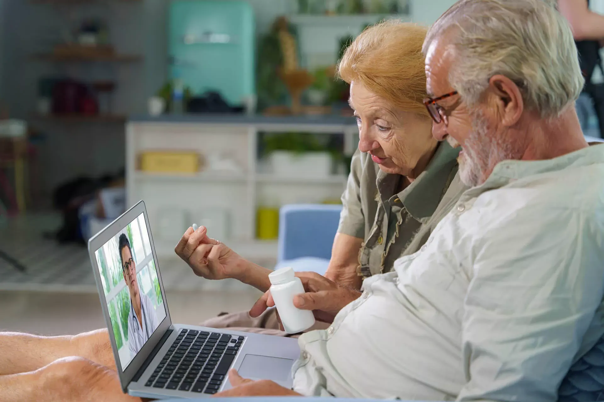 Videosprechstunde: Ein Seniorenpaar sitzt zuhause im Wohnzimmer und spricht mit einem Arzt, den man auf dem Bildschirm eines Laptops sieht. Videosprechstunde: Ein Seniorenpaar sitzt zuhause im Wohnzimmer und spricht mit einem Arzt, den man auf dem Bildschirm eines Laptops sieht.