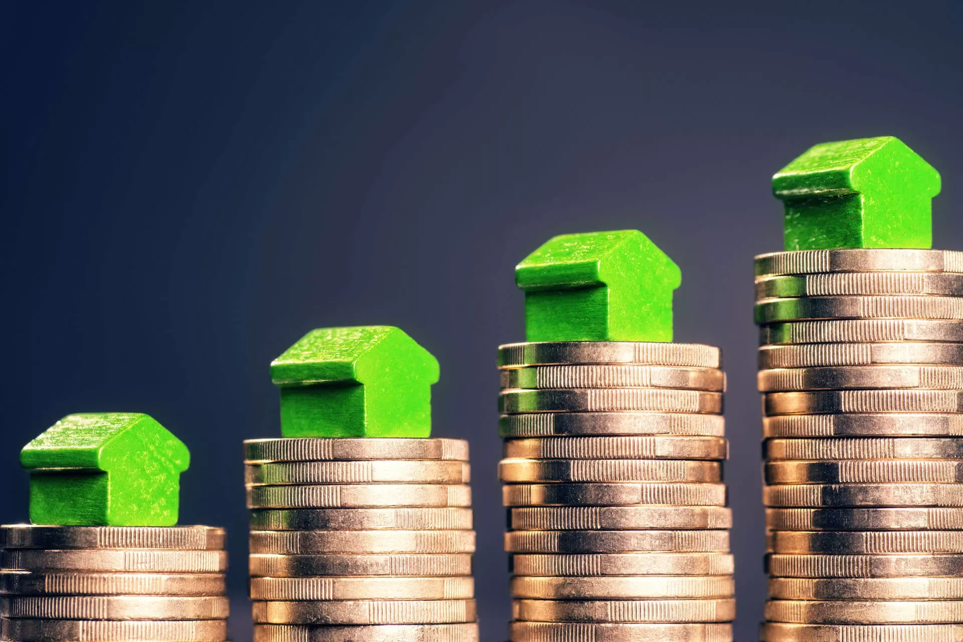 Münzstapel, von links nach rechts ansteigend, auf jedem Stapel steht eine grüne Holzspielfigur in Form eines Hauses. Münzstapel, von links nach rechts ansteigend, auf jedem Stapel steht eine grüne Holzspielfigur in Form eines Hauses.