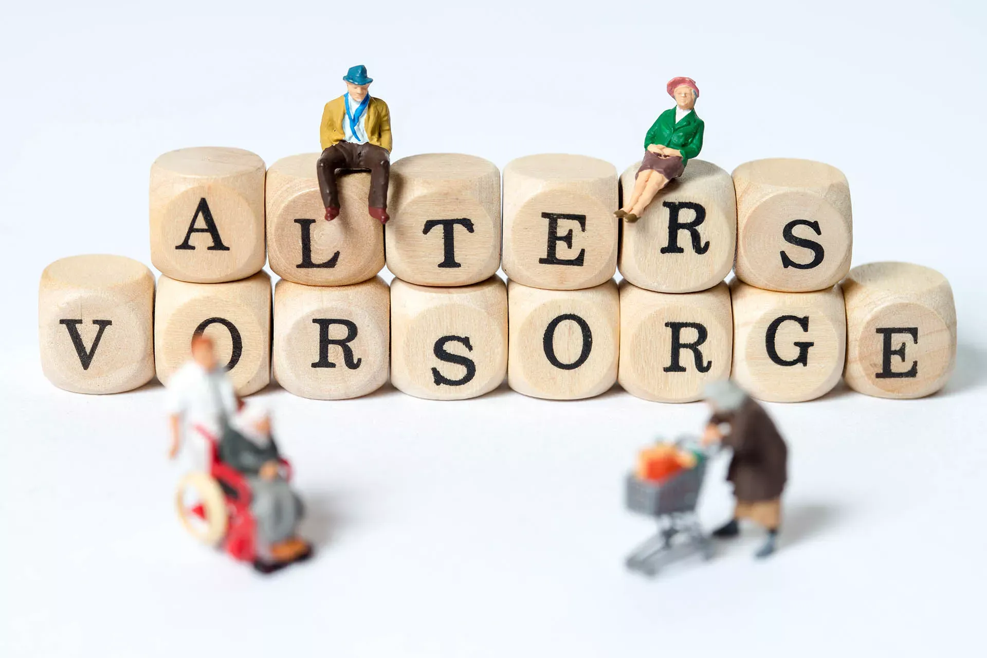 Spielfiguren vor und auf Holzklötzchen mit der Aufschrift: Altersvorsorgee.e. Spielfiguren vor und auf Holzklötzchen mit der Aufschrift: Altersvorsorgee.e.