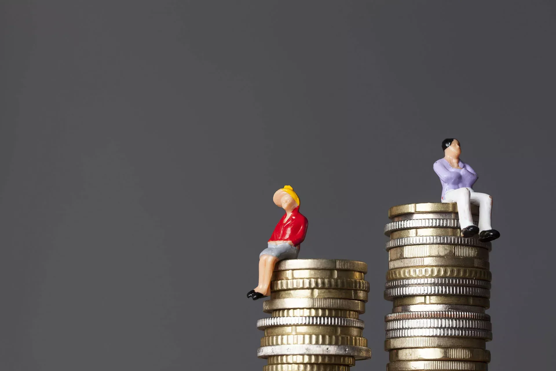 Gender Pay Gap: Figuren von Mann und Frau auf verschieden hohen Münzstapeln. Gender Pay Gap: Figuren von Mann und Frau auf verschieden hohen Münzstapeln.