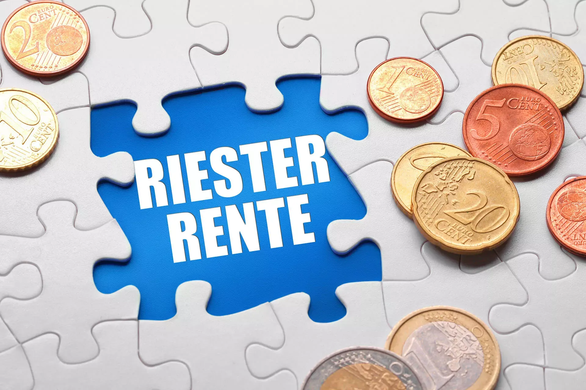 Weißes Puzzle mit Münzen obendrauf, in einer Lücke mit blauem Hintergrund steht Riester-Rente in weißen Buchstaben. Weißes Puzzle mit Münzen obendrauf, in einer Lücke mit blauem Hintergrund steht Riester-Rente in weißen Buchstaben.