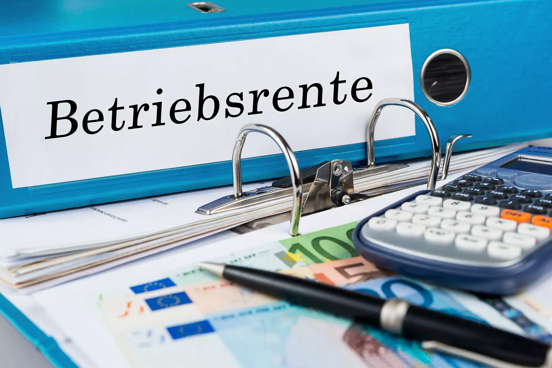 Blauer Aktenordner mit Aufschrift Betriebsrente, davor Taschenrechner, Stift und Geldscheine. Blauer Aktenordner mit Aufschrift Betriebsrente, davor Taschenrechner, Stift und Geldscheine.