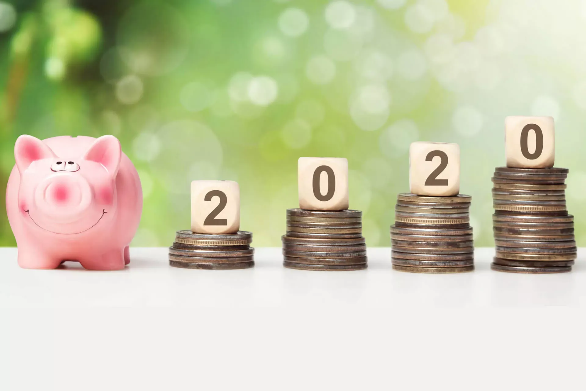 Rosa Sparschwein neben Münztürmen mit Würfeln obenauf, die die Jahreszahl 2020 bilden. Rosa Sparschwein neben Münztürmen mit Würfeln obenauf, die die Jahreszahl 2020 bilden.