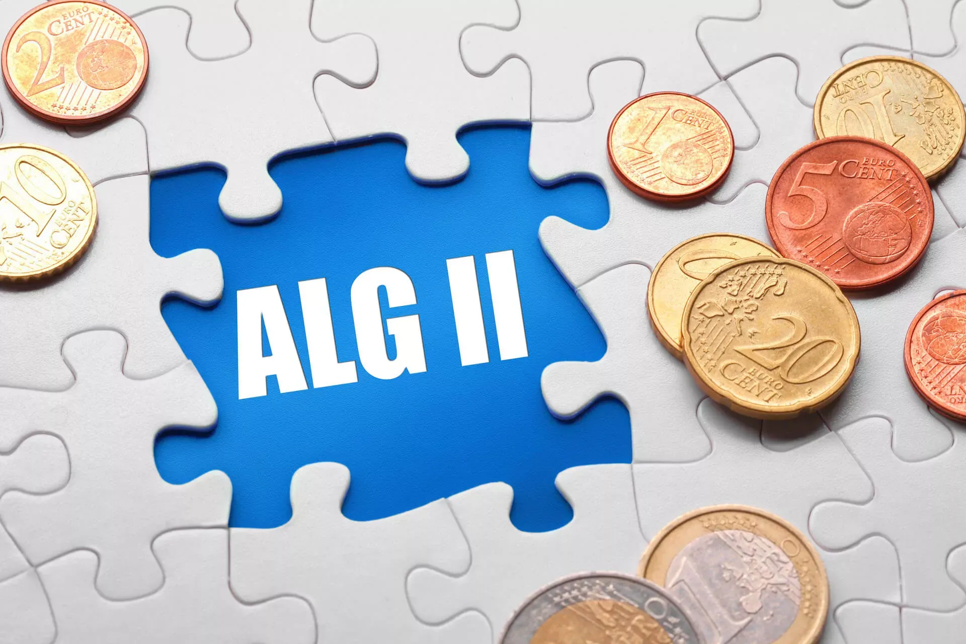 Weißes Puzzle mit Lücke, in der ALG II steht. Darauf liegen Geldmünzen. Weißes Puzzle mit Lücke, in der ALG II steht. Darauf liegen Geldmünzen.