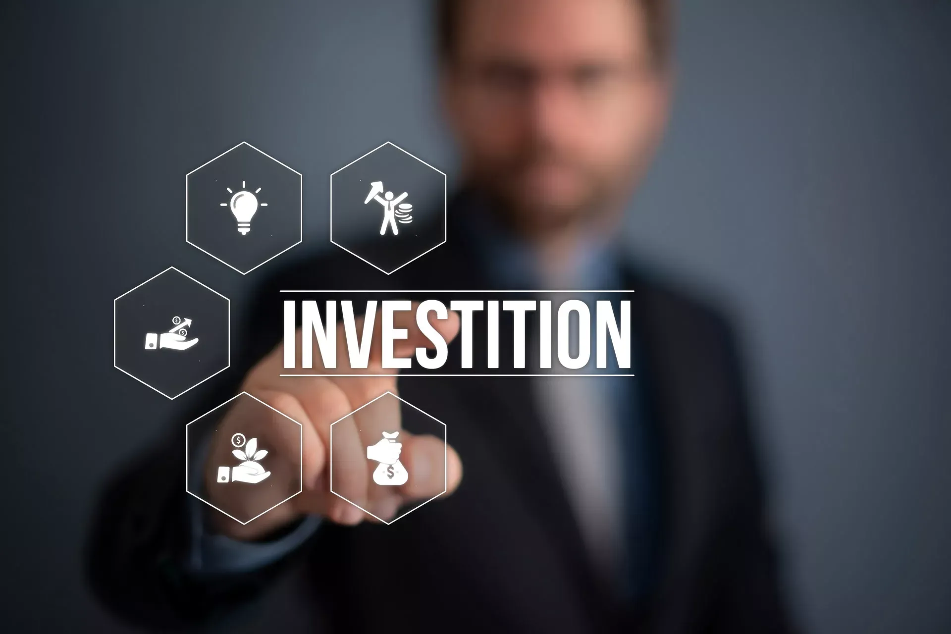 Hand eines Mannes im Hintergrund zeigt auf den Begriff Investition, umrahmt von Wirtschaftssymbolen. Hand eines Mannes im Hintergrund zeigt auf den Begriff Investition, umrahmt von Wirtschaftssymbolen.