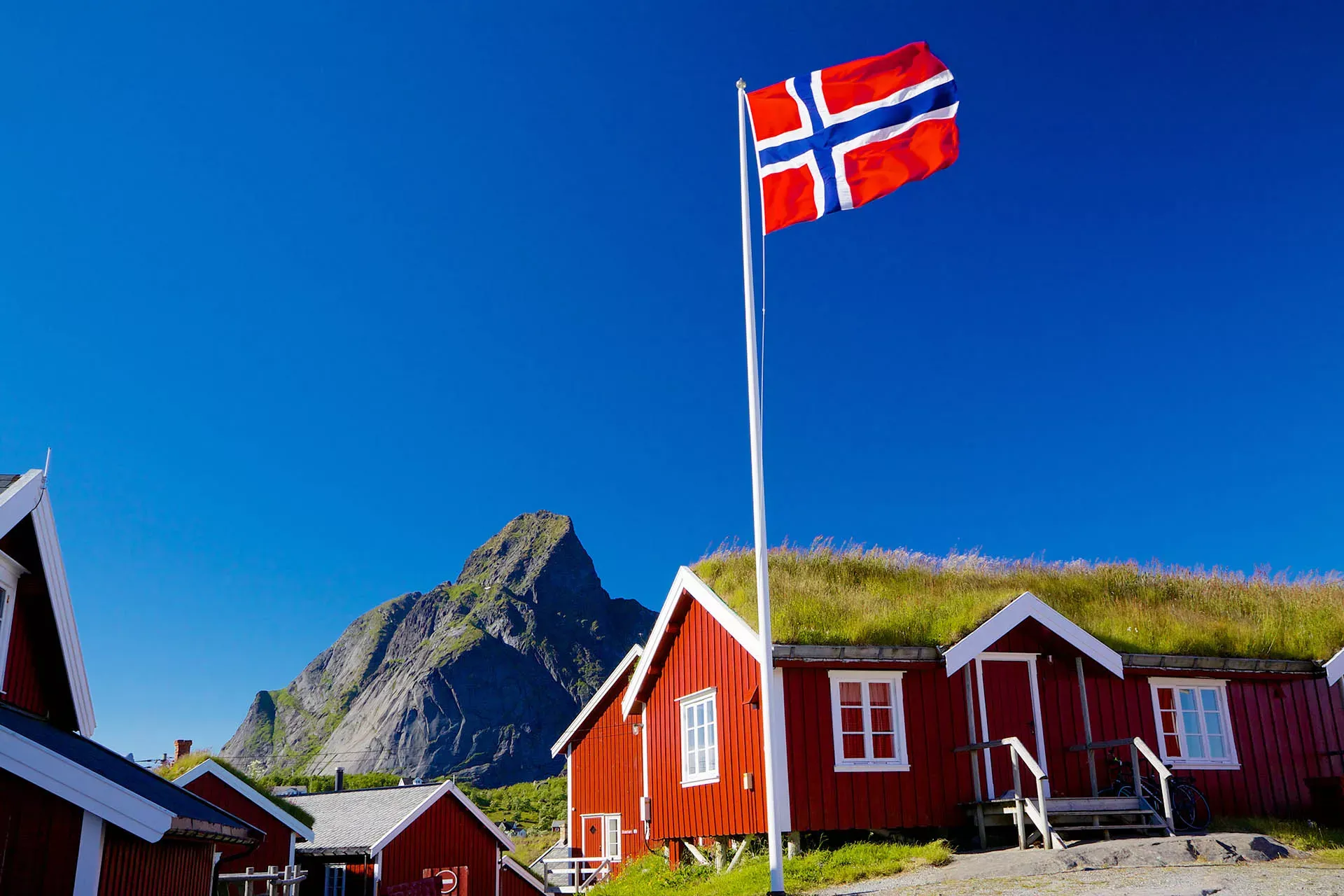 Rot bemalte Häuser vor blauem Himmel mit der Flagge Norwegens. Rot bemalte Häuser vor blauem Himmel mit der Flagge Norwegens.