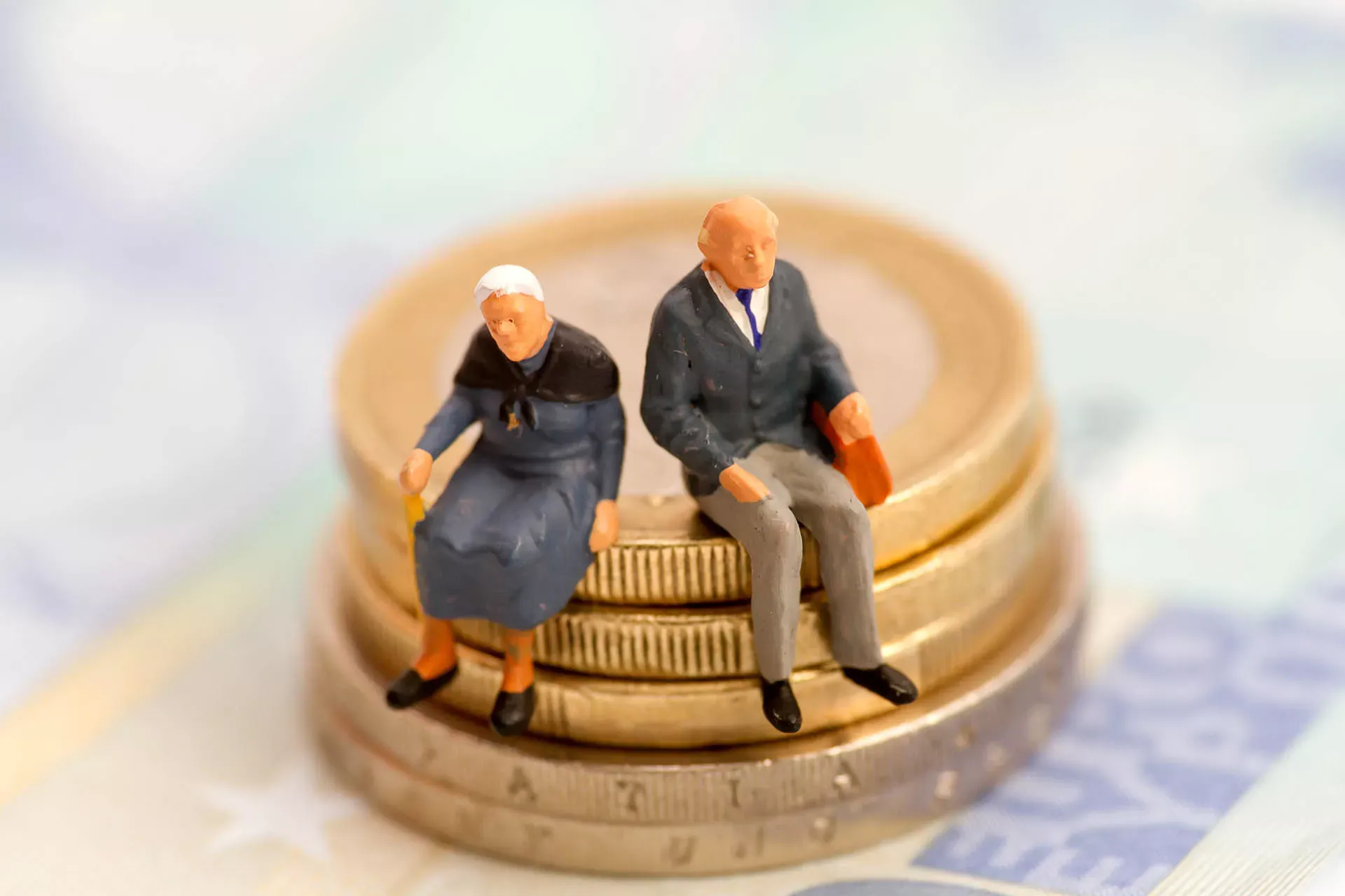 Rentnerpaar als Spielfiguren sitzen auf einem Stapel Geldmünzen. Rentnerpaar als Spielfiguren sitzen auf einem Stapel Geldmünzen.