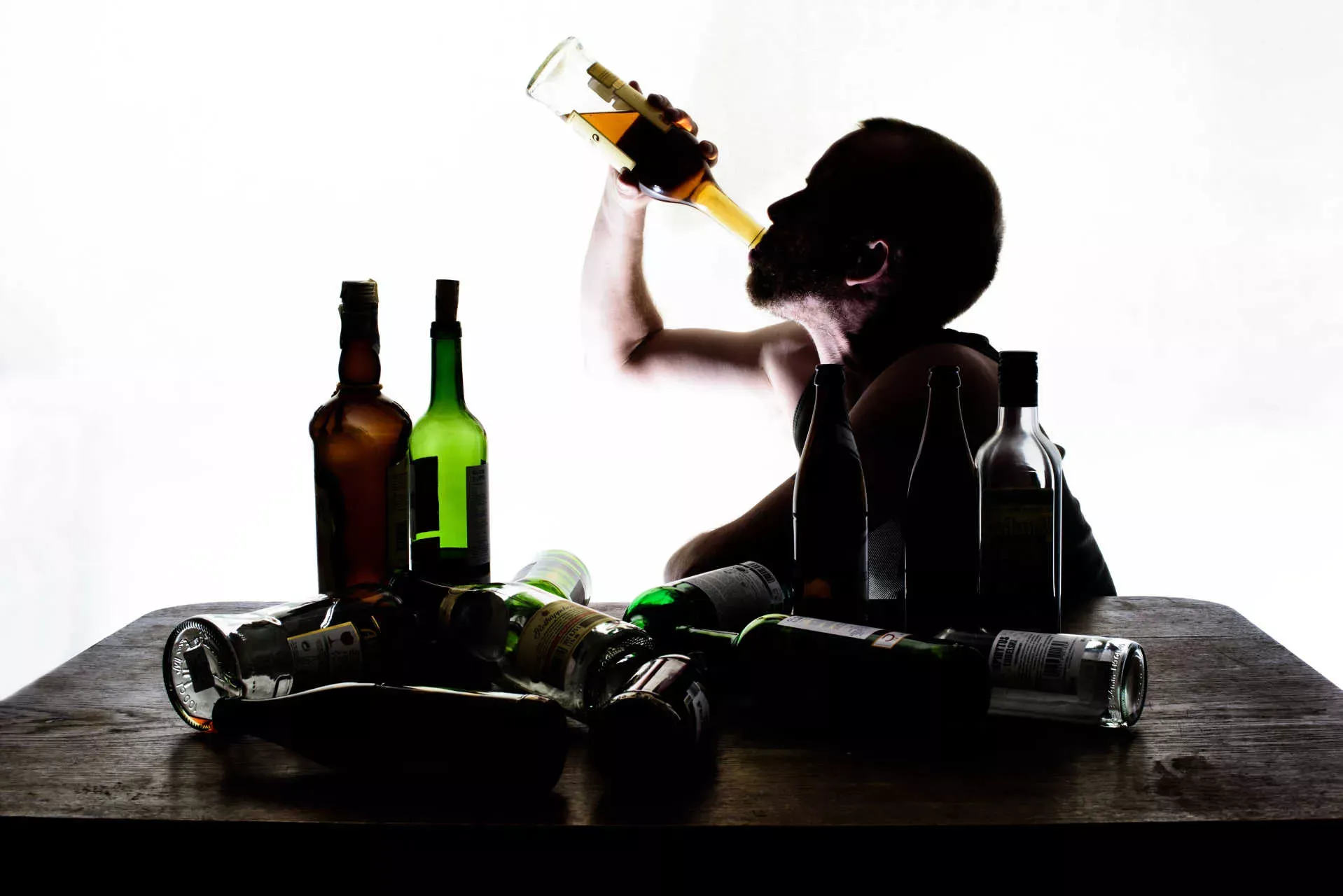 Mann sitzt an Tisch mit leeren Alkoholflaschen und trinkt aus einer Whiskyflasche. Bild: IMAGO / Thomas Eisenhuth Mann sitzt an Tisch mit leeren Alkoholflaschen und trinkt aus einer Whiskyflasche. Bild: IMAGO / Thomas Eisenhuth