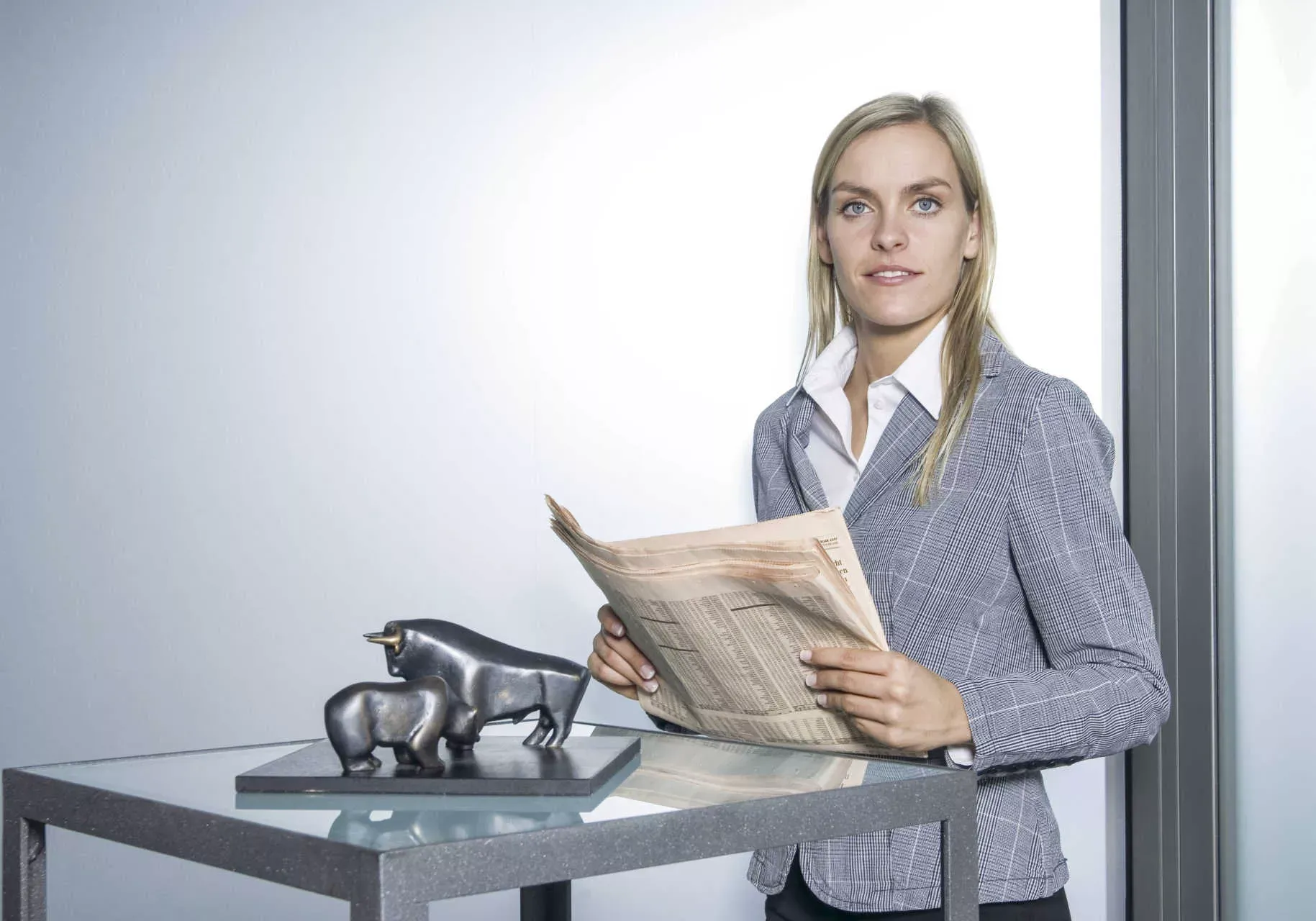 Frau steht mit Aktienzeitung vor Tisch mit Bulle und Bär. Bild: IMAGO / allOver-MEV / imago stock&people Frau steht mit Aktienzeitung vor Tisch mit Bulle und Bär. Bild: IMAGO / allOver-MEV / imago stock&people
