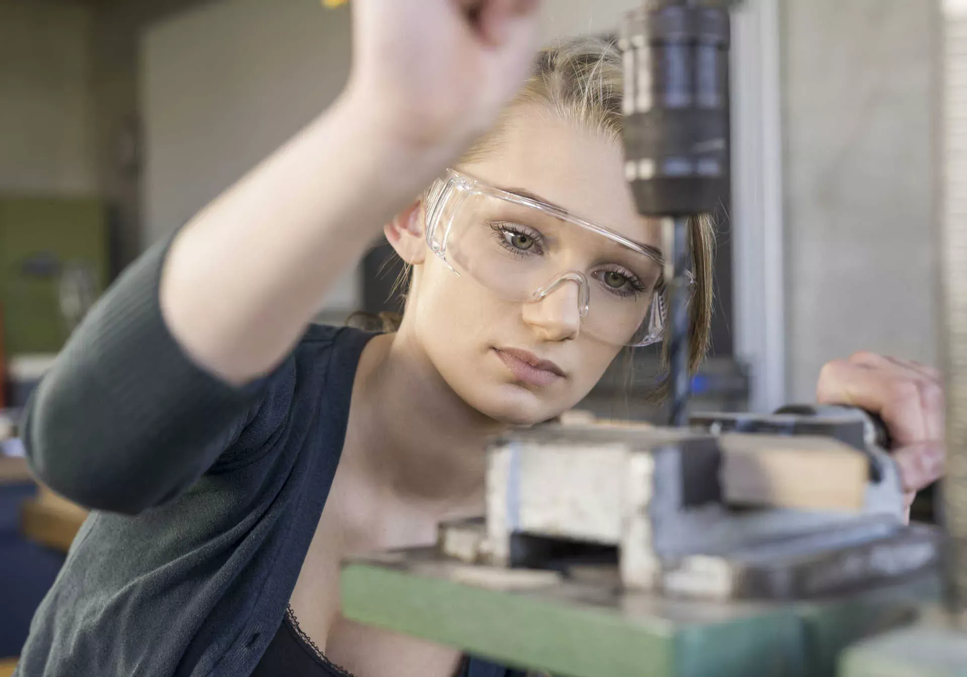 Jugendliche Auszubildende steht mit Schutzbrille in einer Werkstatt an einer Bohrmaschine. Bild: IMAGO / allOver-MEV Jugendliche Auszubildende steht mit Schutzbrille in einer Werkstatt an einer Bohrmaschine. Bild: IMAGO / allOver-MEV