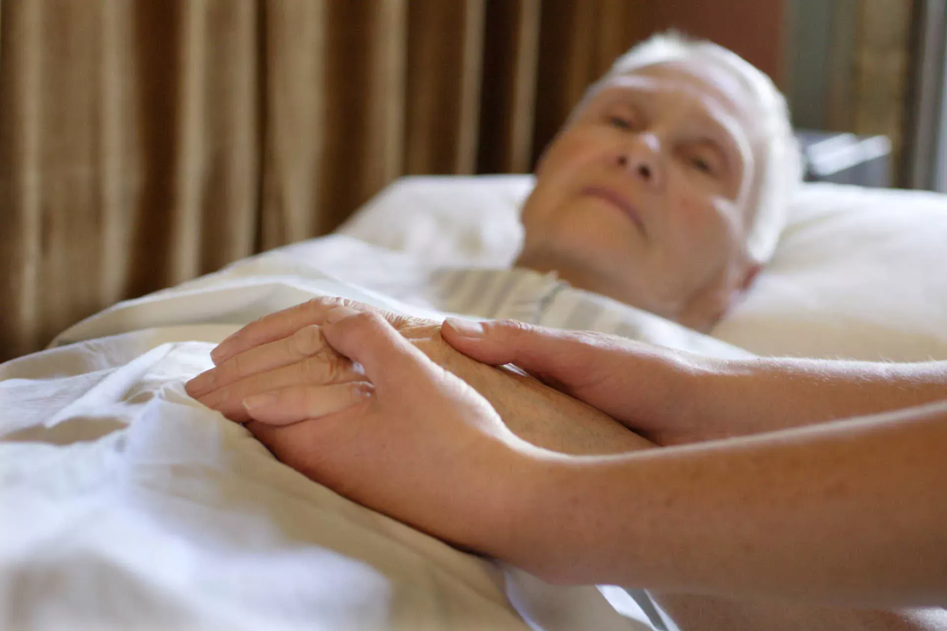 Seniorin liegt im Bett, Pflegeperson hält ihre Hand. Bild: IMAGO / photothek / Ute Grabowsky Seniorin liegt im Bett, Pflegeperson hält ihre Hand. Bild: IMAGO / photothek / Ute Grabowsky