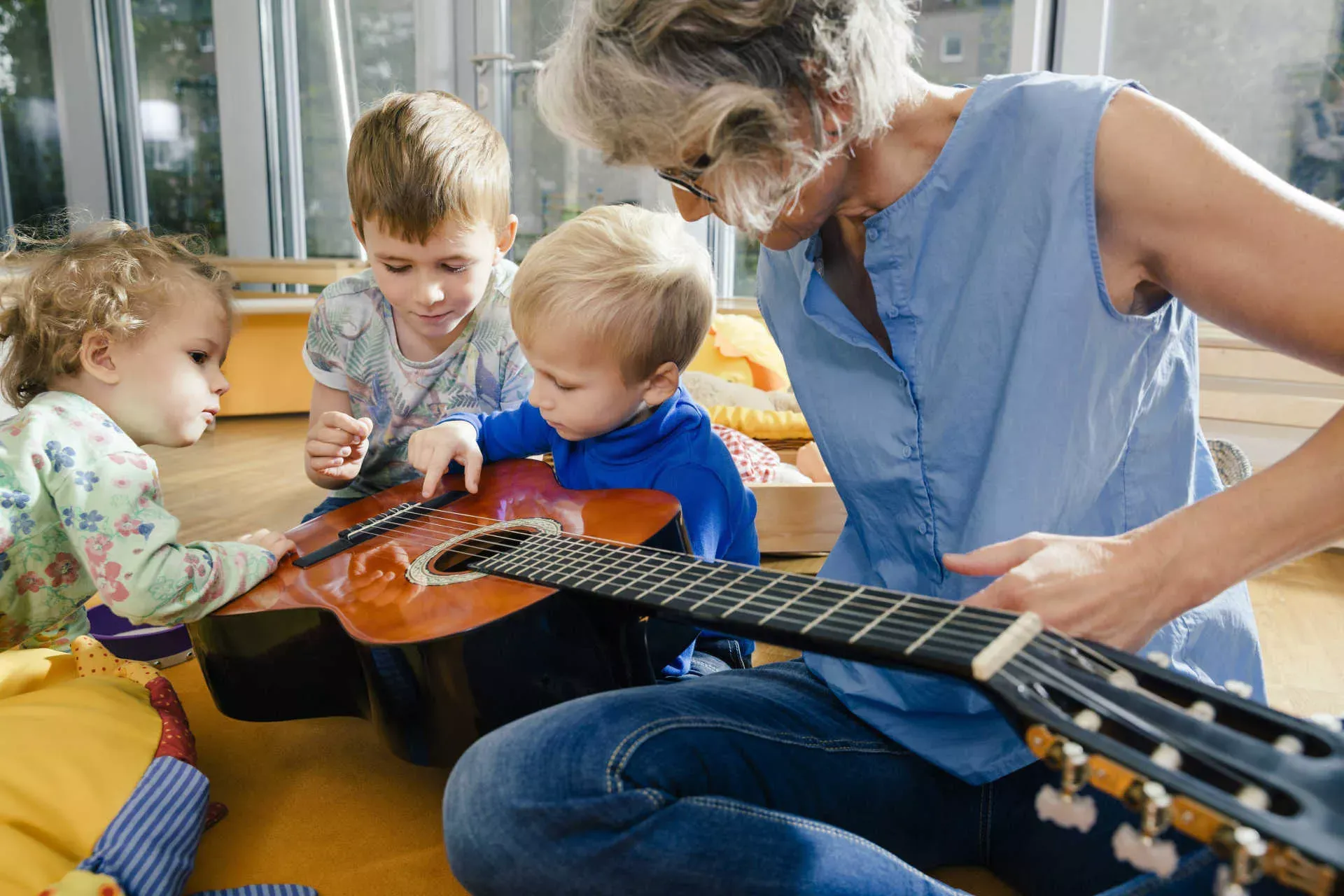 Ältere Erzieherin in der Kita zeigt Kindern eine Gitarre. Bild: IMAGO / Westend61 / Mareen Fischinger Ältere Erzieherin in der Kita zeigt Kindern eine Gitarre. Bild: IMAGO / Westend61 / Mareen Fischinger