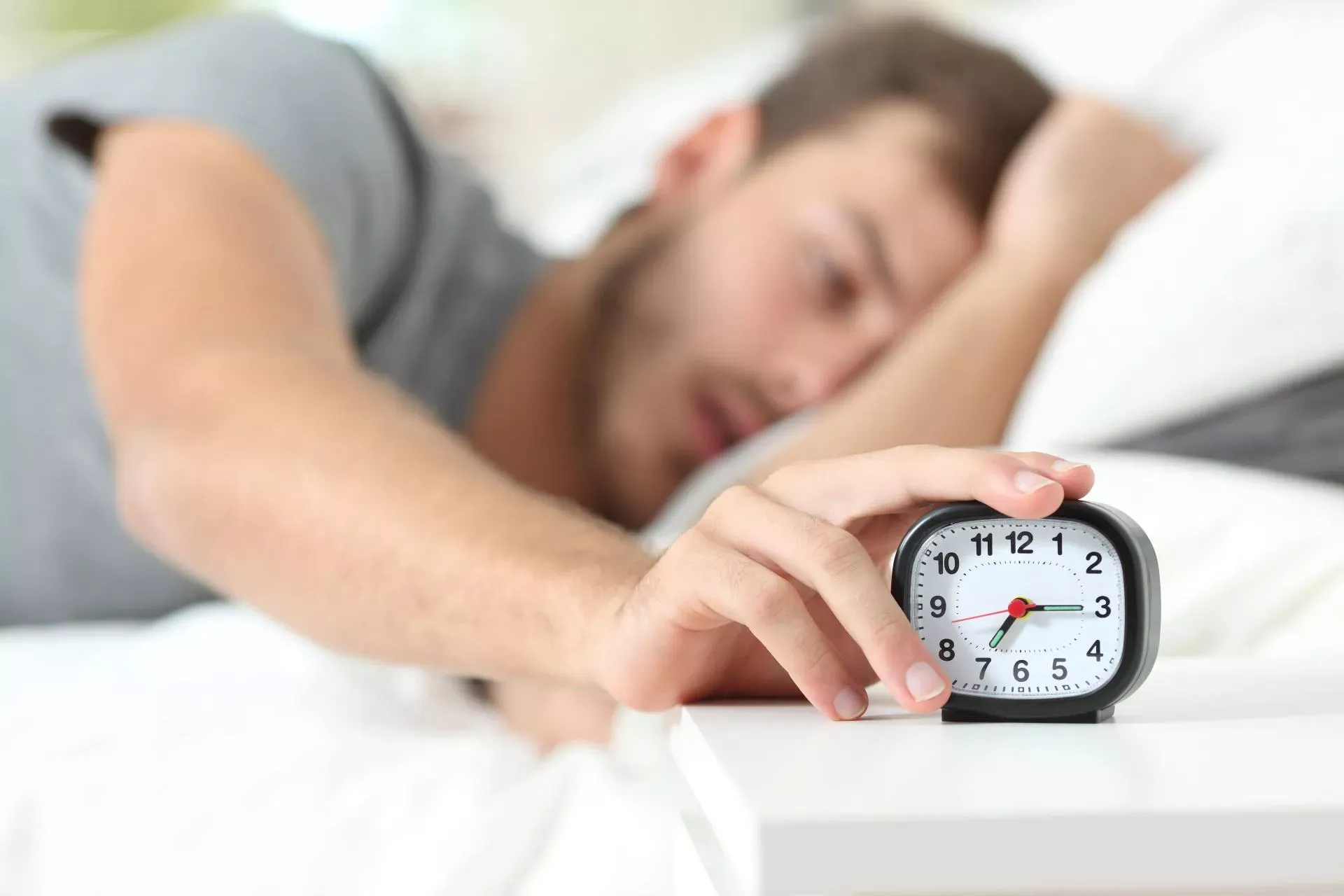 Mann im Bett liegend schaltet seinen Wecker aus. Bild: IMAGO / Antonio Guillem / Panthermedia Mann im Bett liegend schaltet seinen Wecker aus. Bild: IMAGO / Antonio Guillem / Panthermedia