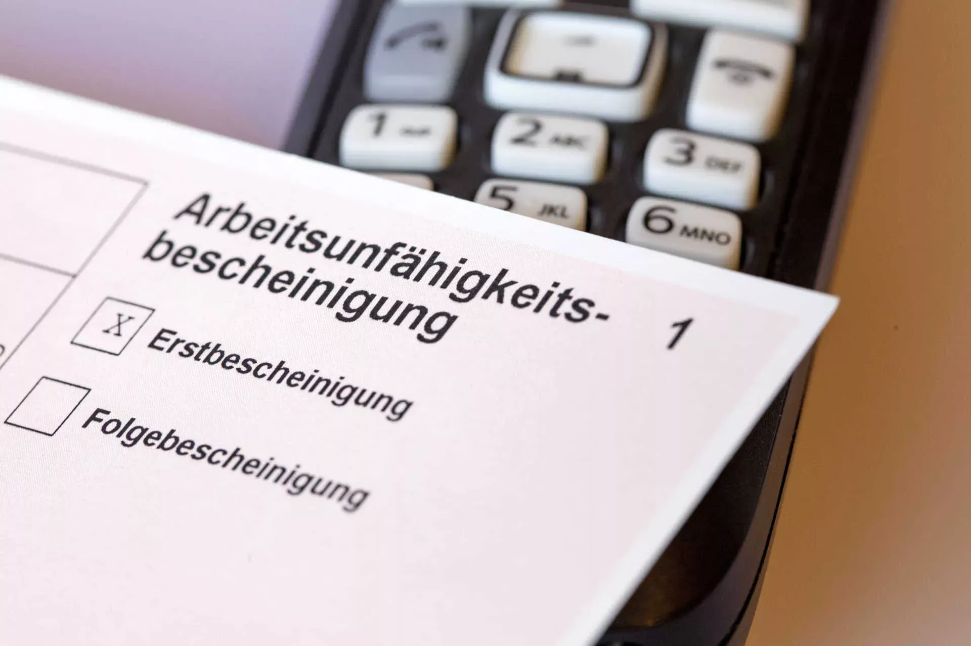 Arbeitsunfähigkeitsbescheinigung liegt auf Telefon. Bild: IMAGO / Future Image / Robert Schmiegelt Arbeitsunfähigkeitsbescheinigung liegt auf Telefon. Bild: IMAGO / Future Image / Robert Schmiegelt
