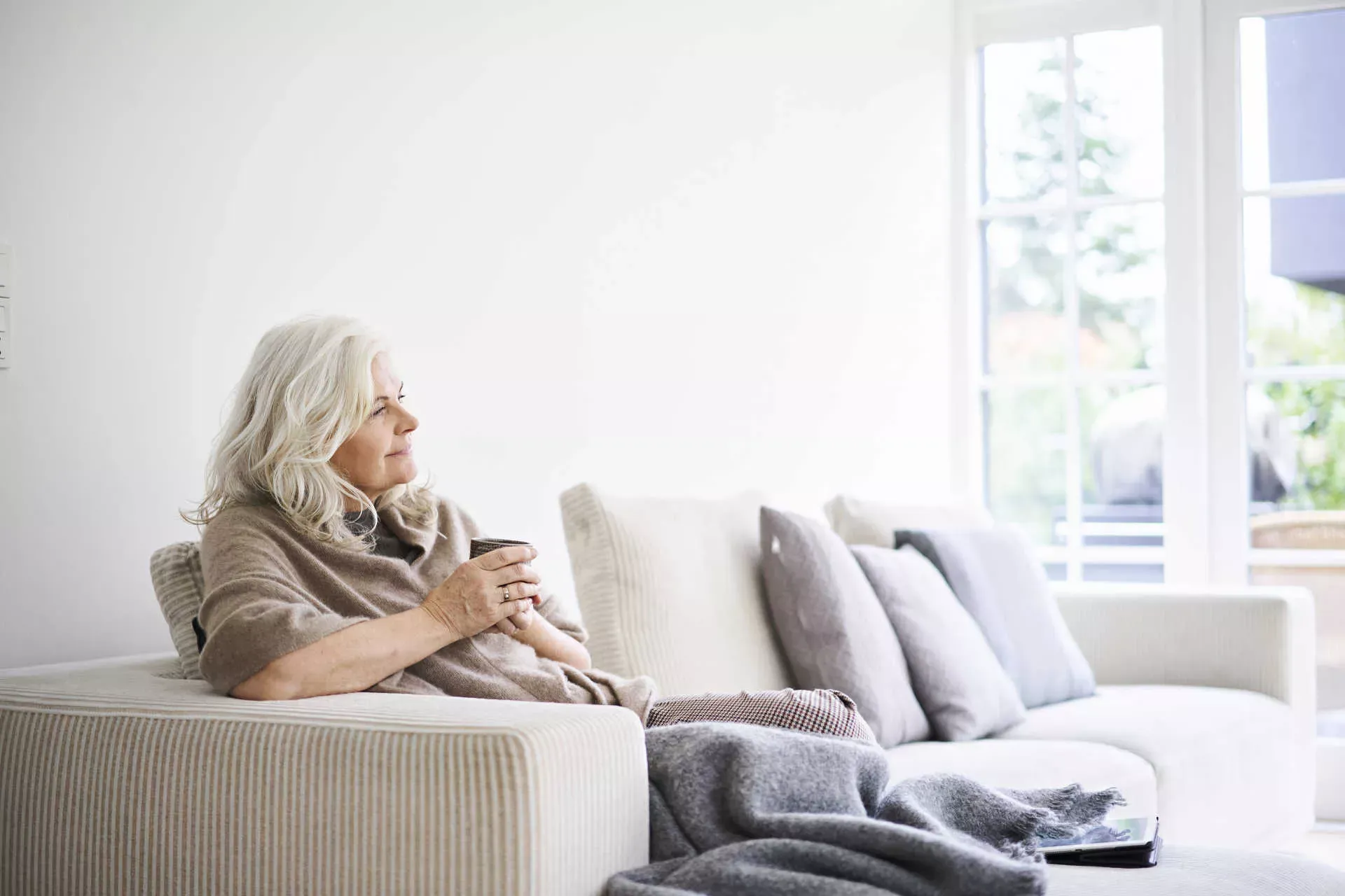 Ältere Frau sitzt mit Tasse in der Hand gedankenvoll auf ihrem Sofa. Bild: IMAGO / Westend61 / Jakob Helbig Ältere Frau sitzt mit Tasse in der Hand gedankenvoll auf ihrem Sofa. Bild: IMAGO / Westend61 / Jakob Helbig