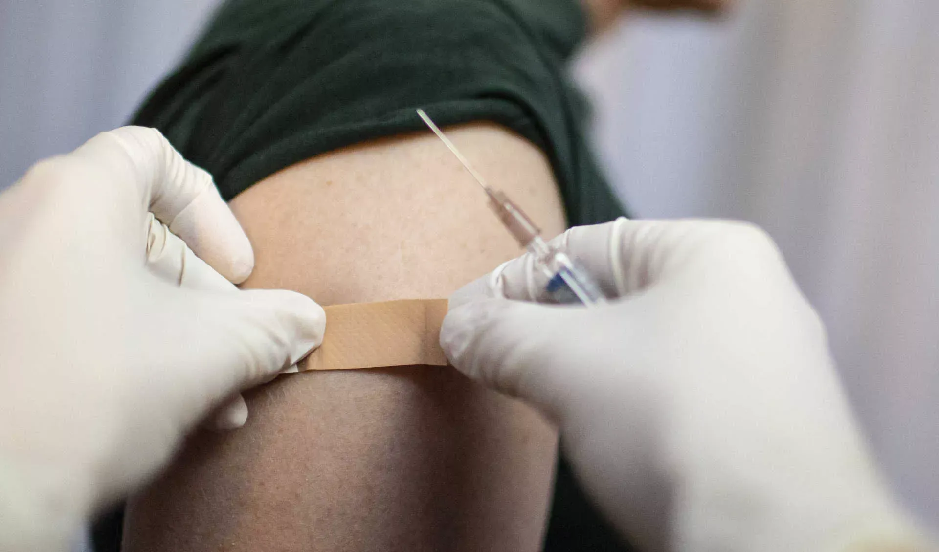 Arzt mit Spritze klebt Pflaster auf Oberarm von Patient. Bild: IMAGO / photothek / Ute Grabowsky Arzt mit Spritze klebt Pflaster auf Oberarm von Patient. Bild: IMAGO / photothek / Ute Grabowsky