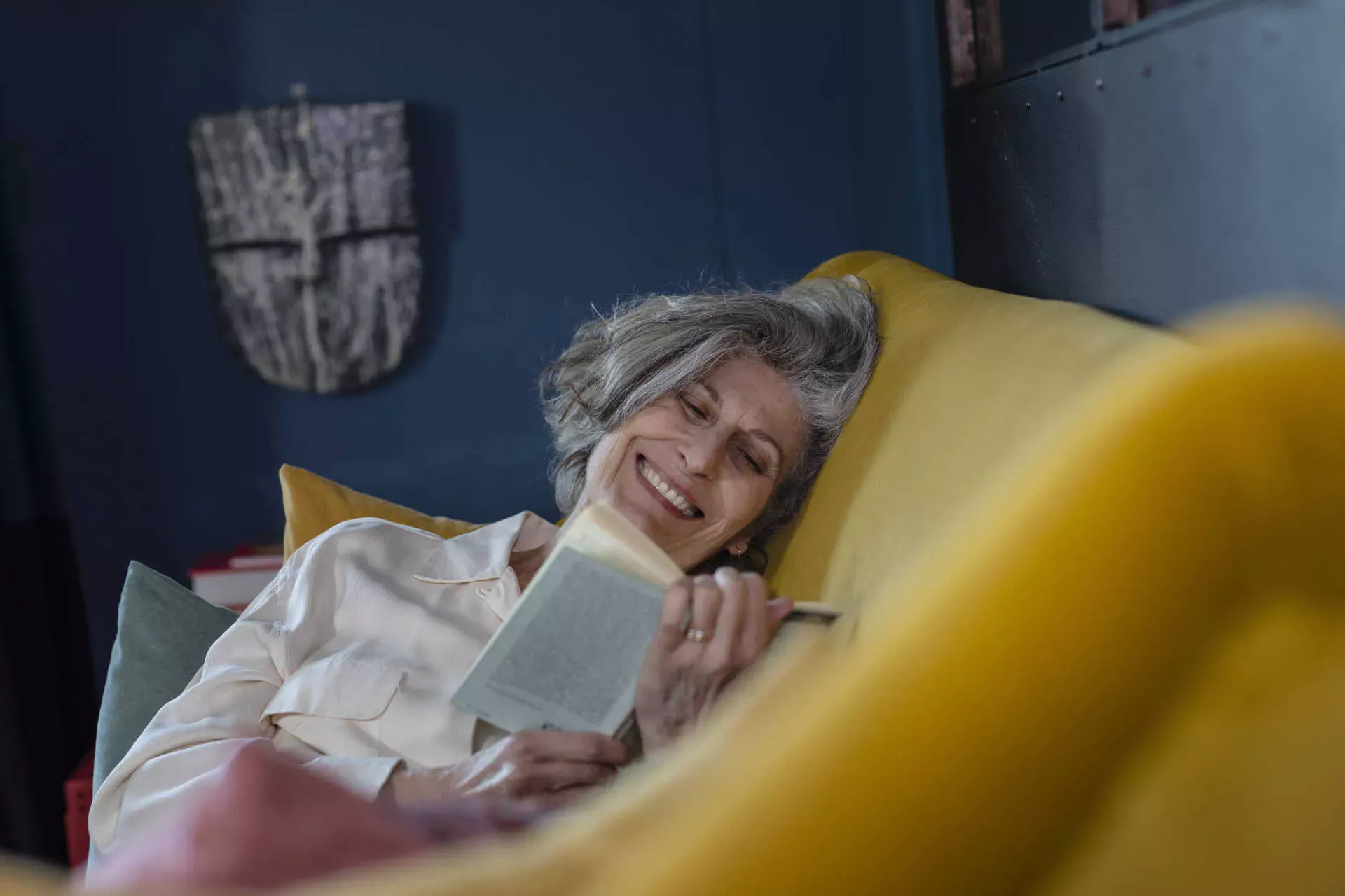 Seniorin liegt auf dem Sofa und liest lächelnd ein Buch. Bild: IMAGO / Westend61 / Emma Innocenti Seniorin liegt auf dem Sofa und liest lächelnd ein Buch. Bild: IMAGO / Westend61 / Emma Innocenti