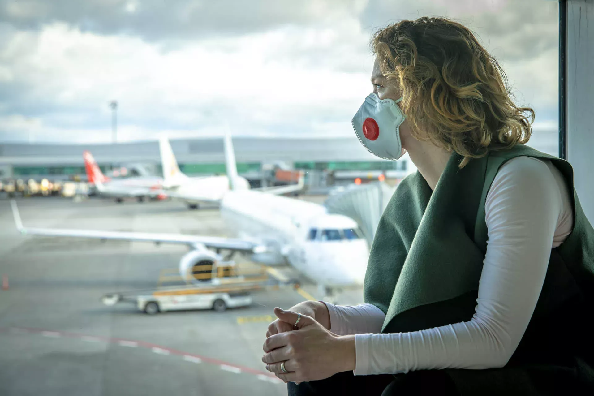 Frau mit FFP2-Maske schaut aus Flughafenfenster auf Flugzeuge. Bild: IMAGO / Panthermedia / Eduard Goričev Frau mit FFP2-Maske schaut aus Flughafenfenster auf Flugzeuge. Bild: IMAGO / Panthermedia / Eduard Goričev