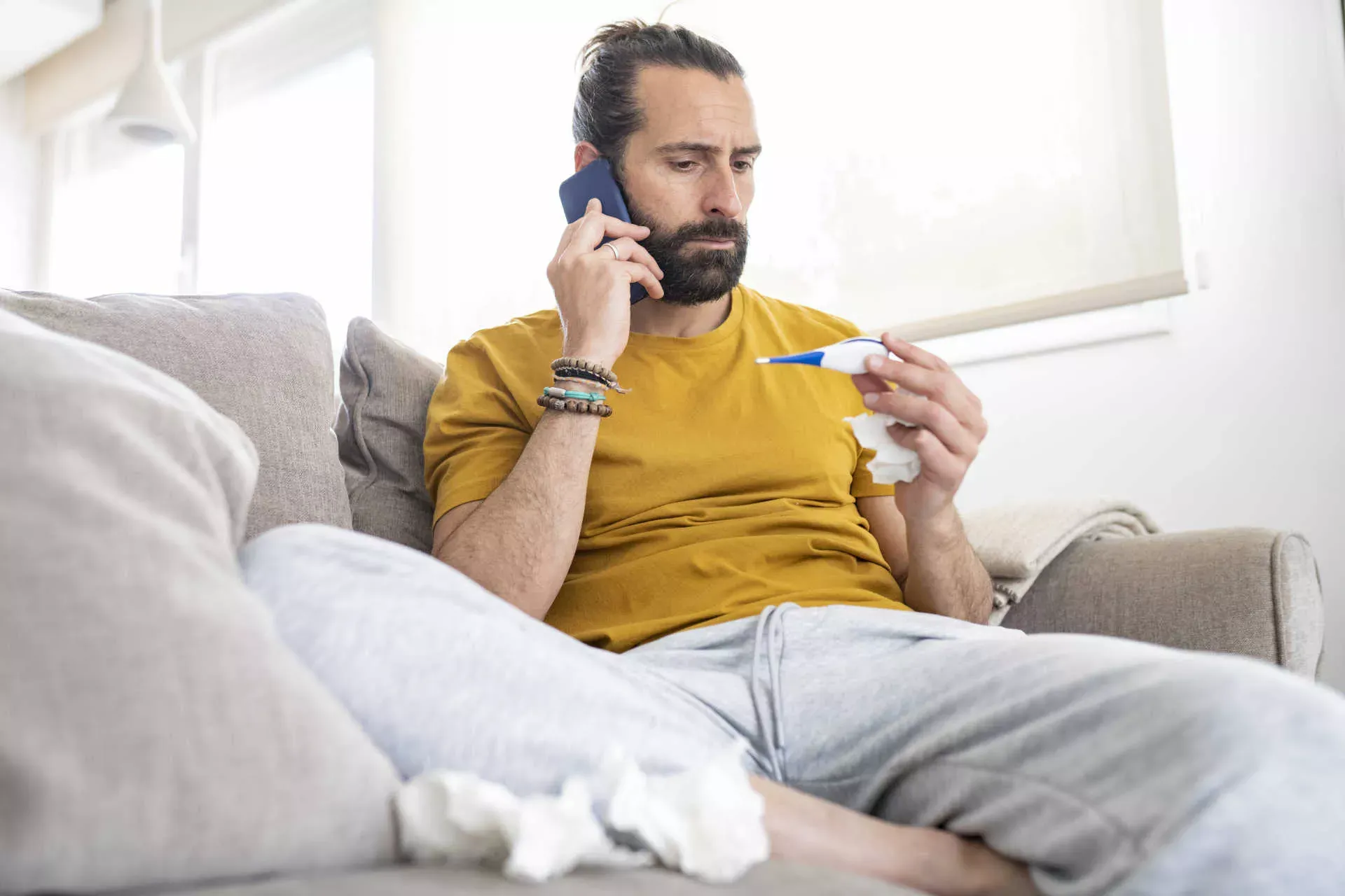 Mann mit Erkältung sitzt auf dem Sofa mit Fieberthermometer in der Hand und telefoniert.Bild: IMAGO / Westend61 / Jose Carlos Ichi Mann mit Erkältung sitzt auf dem Sofa mit Fieberthermometer in der Hand und telefoniert.Bild: IMAGO / Westend61 / Jose Carlos Ichi