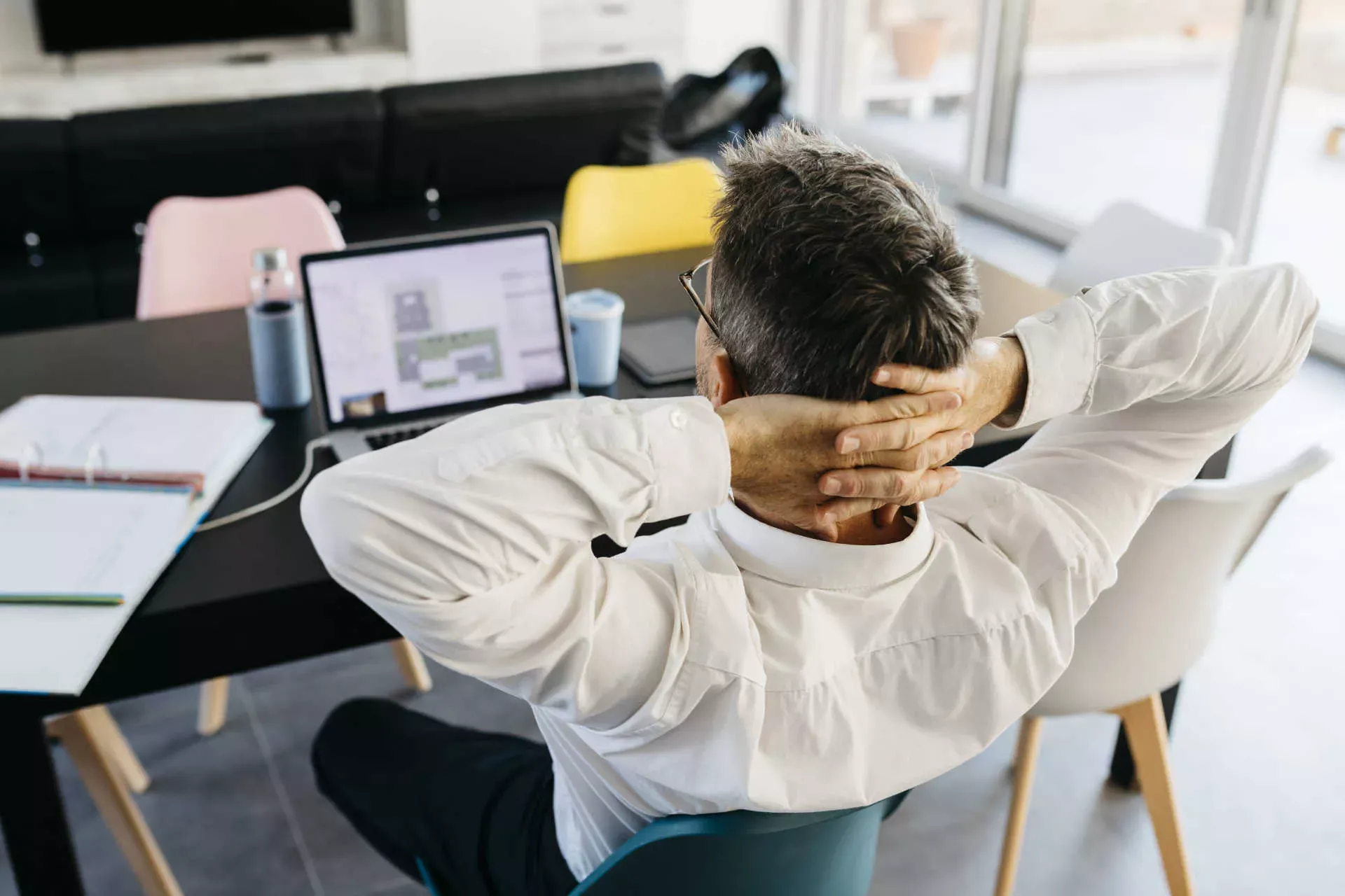 Mann im Homeoffice sitzt am Esstisch vor seinem Notebook und entspannt mit hinter dem Kopf verschraenkten Arme. Bild: IMAGO / Westend61 / Josep Rovirosa Mann im Homeoffice sitzt am Esstisch vor seinem Notebook und entspannt mit hinter dem Kopf verschraenkten Arme. Bild: IMAGO / Westend61 / Josep Rovirosa