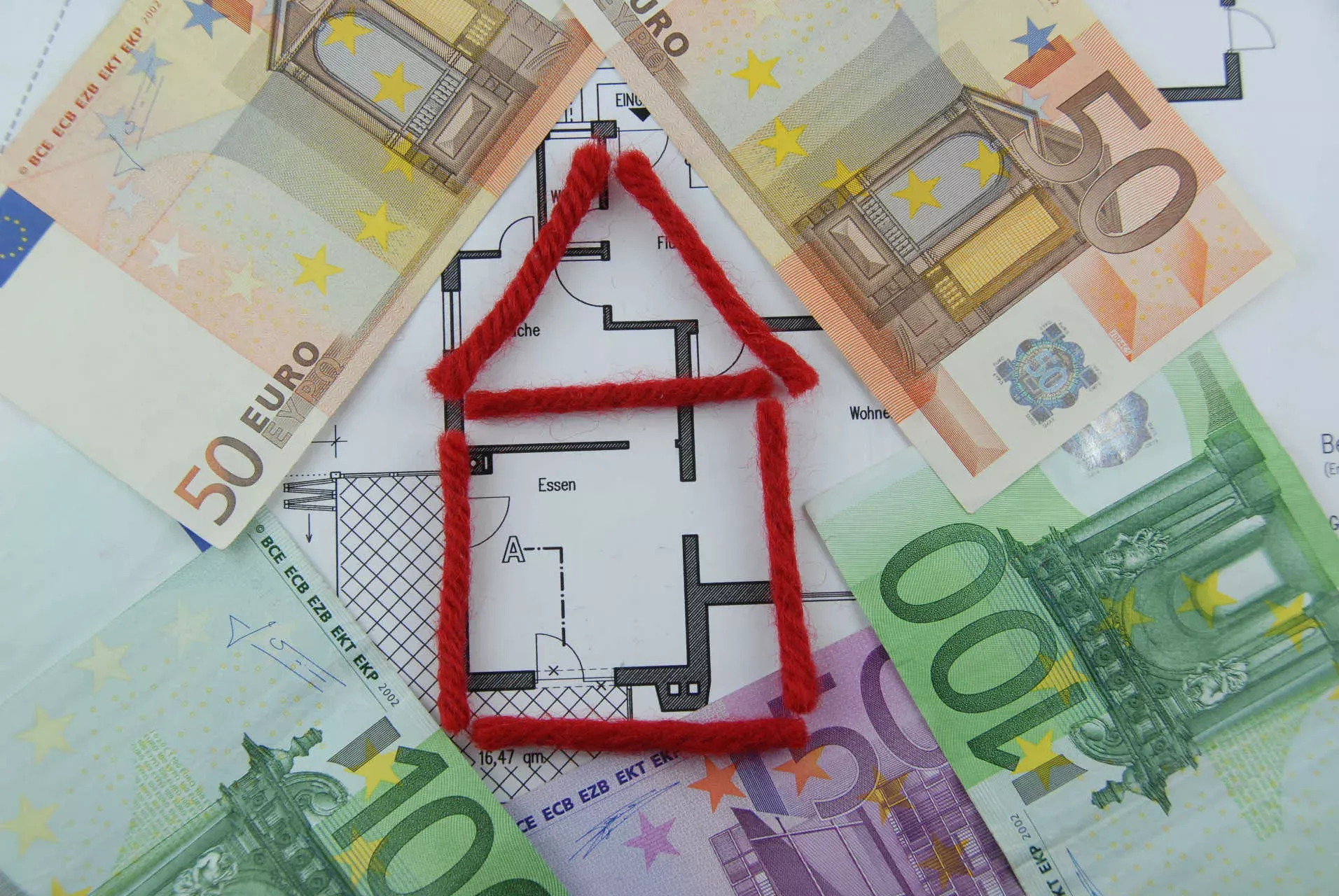 Hausmodell aus roter Wolle auf Bauplan, umgeben von Euro-Geldscheinen. Bild: IMAGO / Panthermedia / Stefan Trux Hausmodell aus roter Wolle auf Bauplan, umgeben von Euro-Geldscheinen. Bild: IMAGO / Panthermedia / Stefan Trux