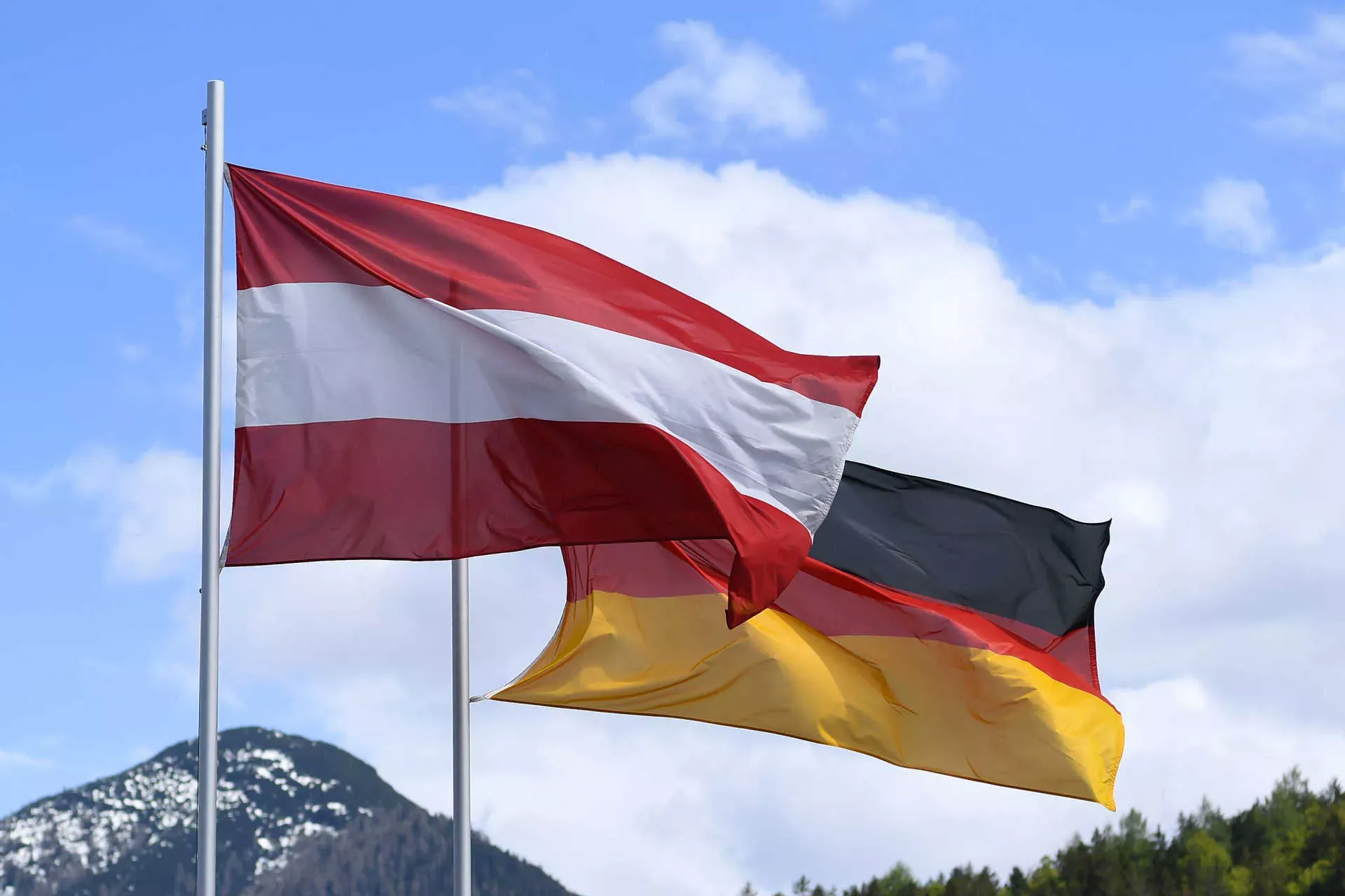 Flaggen von Deutschland und Österreich wehen im Wind vor blauem Himmel mit Bergkulisse. Bild: IMAGO / Revierfoto Flaggen von Deutschland und Österreich wehen im Wind vor blauem Himmel mit Bergkulisse. Bild: IMAGO / Revierfoto