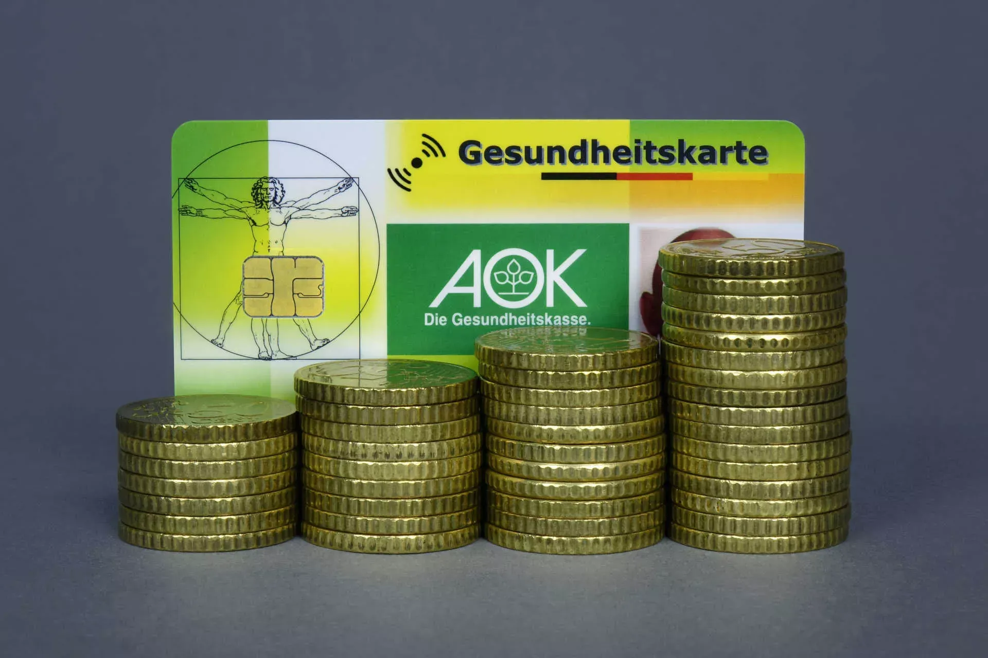 Gesundheitskarte hinter ansteigenden Stapeln von Geldmünzen. Bild: IMAGO / Steinach Gesundheitskarte hinter ansteigenden Stapeln von Geldmünzen. Bild: IMAGO / Steinach