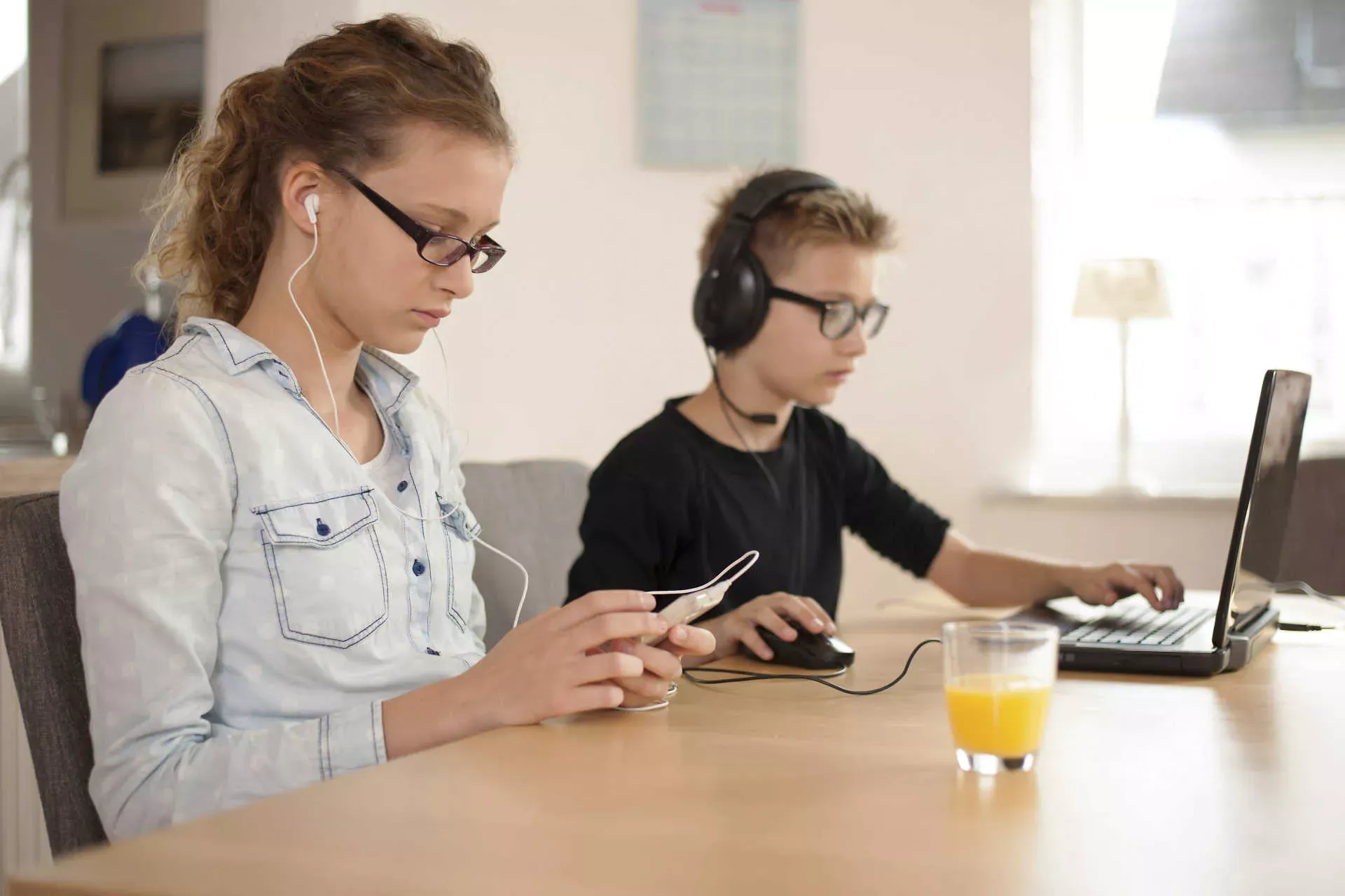 Jugendliche und Kind sitzen an einem Tisch mit Kopfhörern am Smartphone und Computer. Bild: IMAGO / Westend61 Jugendliche und Kind sitzen an einem Tisch mit Kopfhörern am Smartphone und Computer. Bild: IMAGO / Westend61