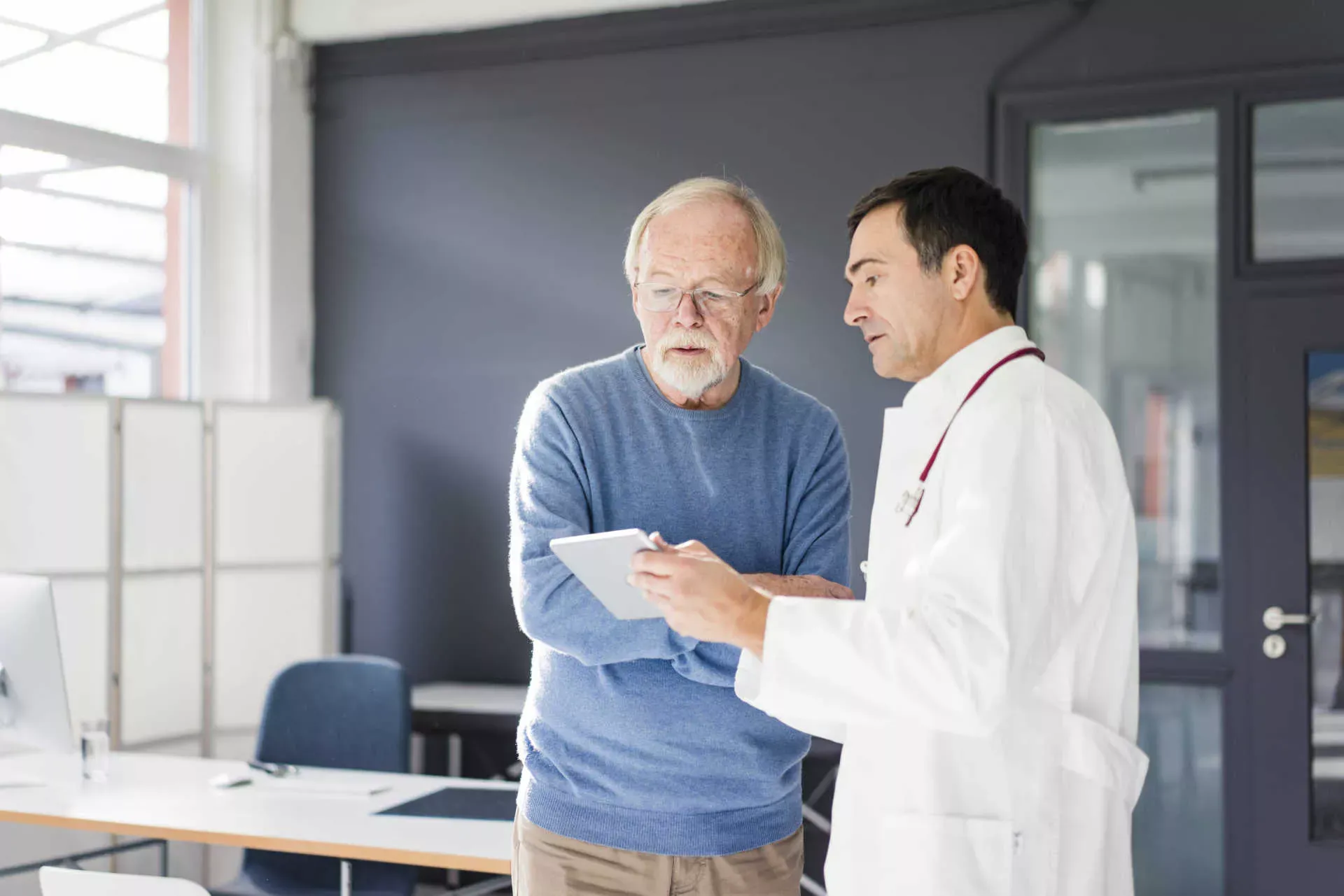 Arzt steht mit älterem Patienten in der Praxis und zeigt ein Tablet. Bild: IMAGO / Westend61 / Joseffson Arzt steht mit älterem Patienten in der Praxis und zeigt ein Tablet. Bild: IMAGO / Westend61 / Joseffson
