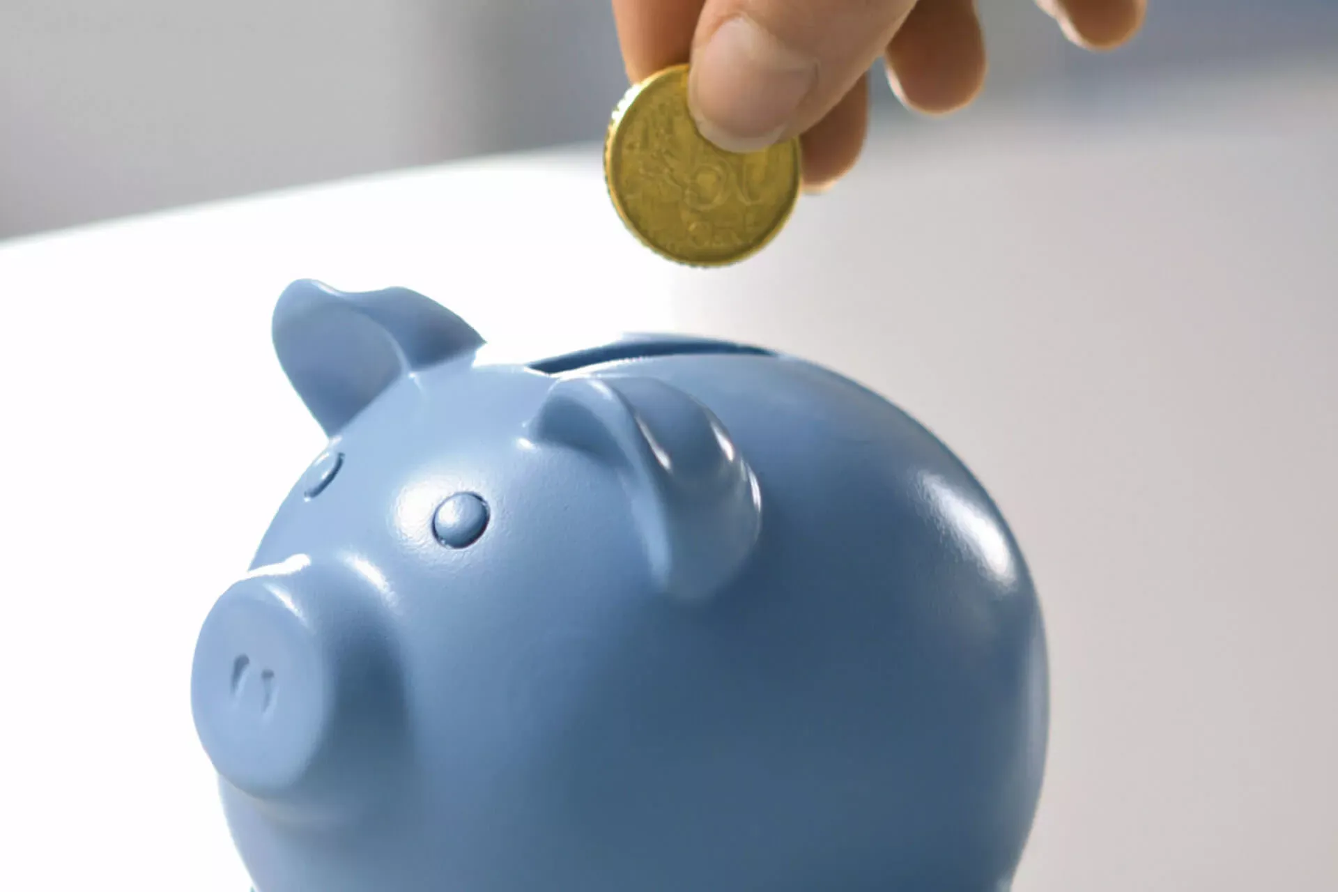 Frauenhand steckt eine 50-Cent-Münze in ein blaues Sparschwein. Frauenhand steckt eine 50-Cent-Münze in ein blaues Sparschwein.