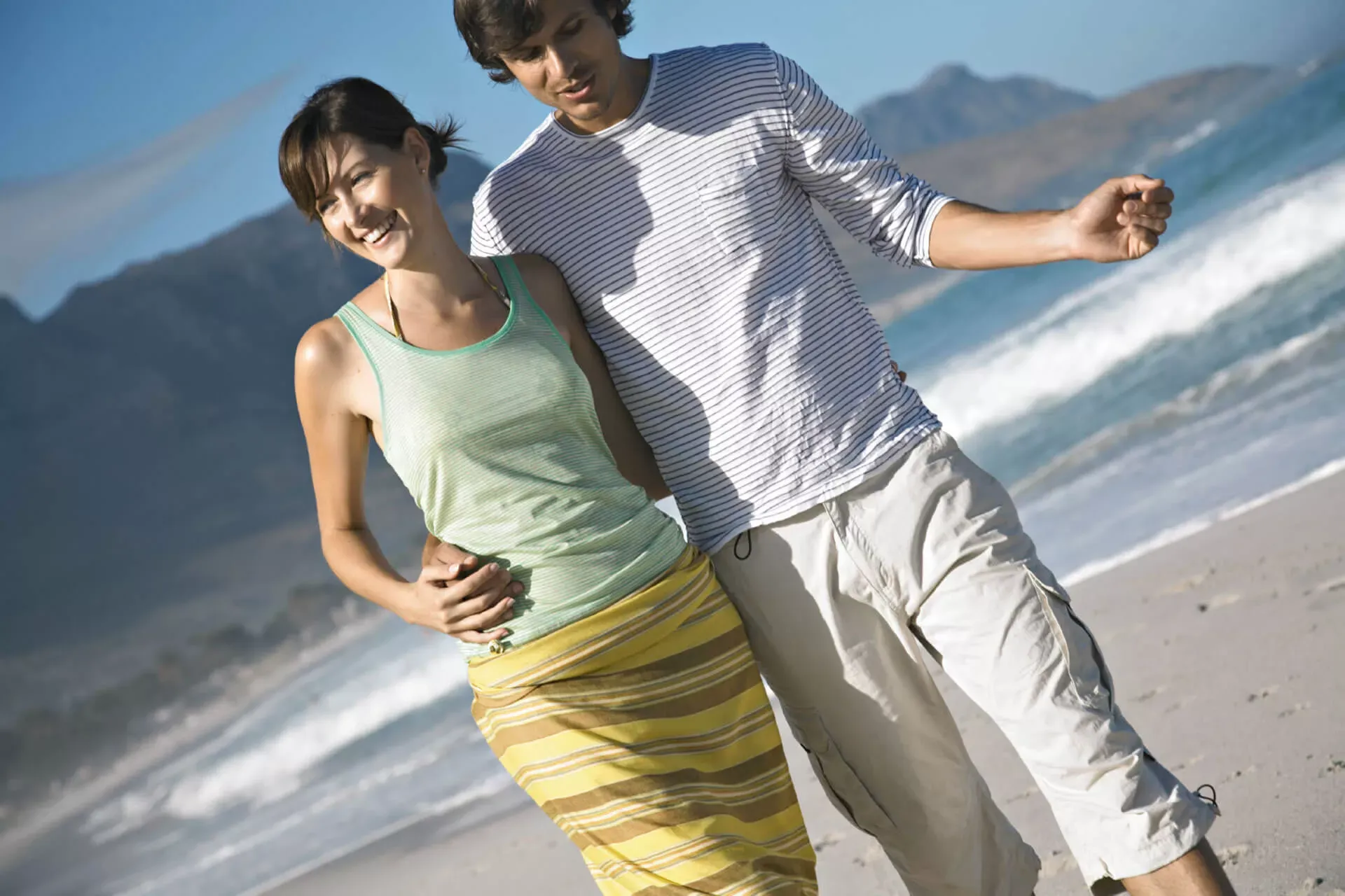 Junges Paar geht Arm in Arm am Strand spazieren. Junges Paar geht Arm in Arm am Strand spazieren.