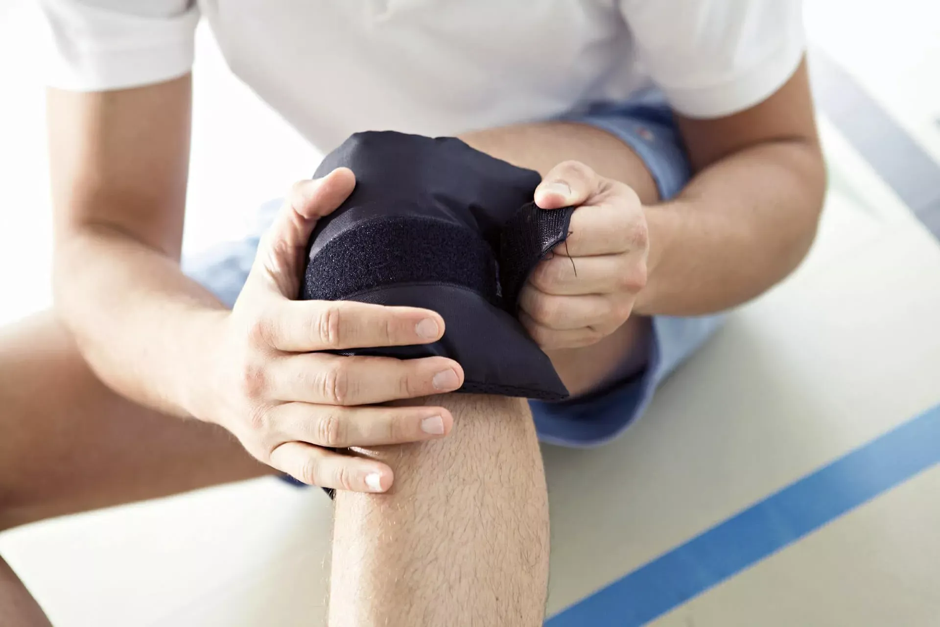 Verletzer Mann in Sporthalle legt sich eine Kniebandage an. Verletzer Mann in Sporthalle legt sich eine Kniebandage an.