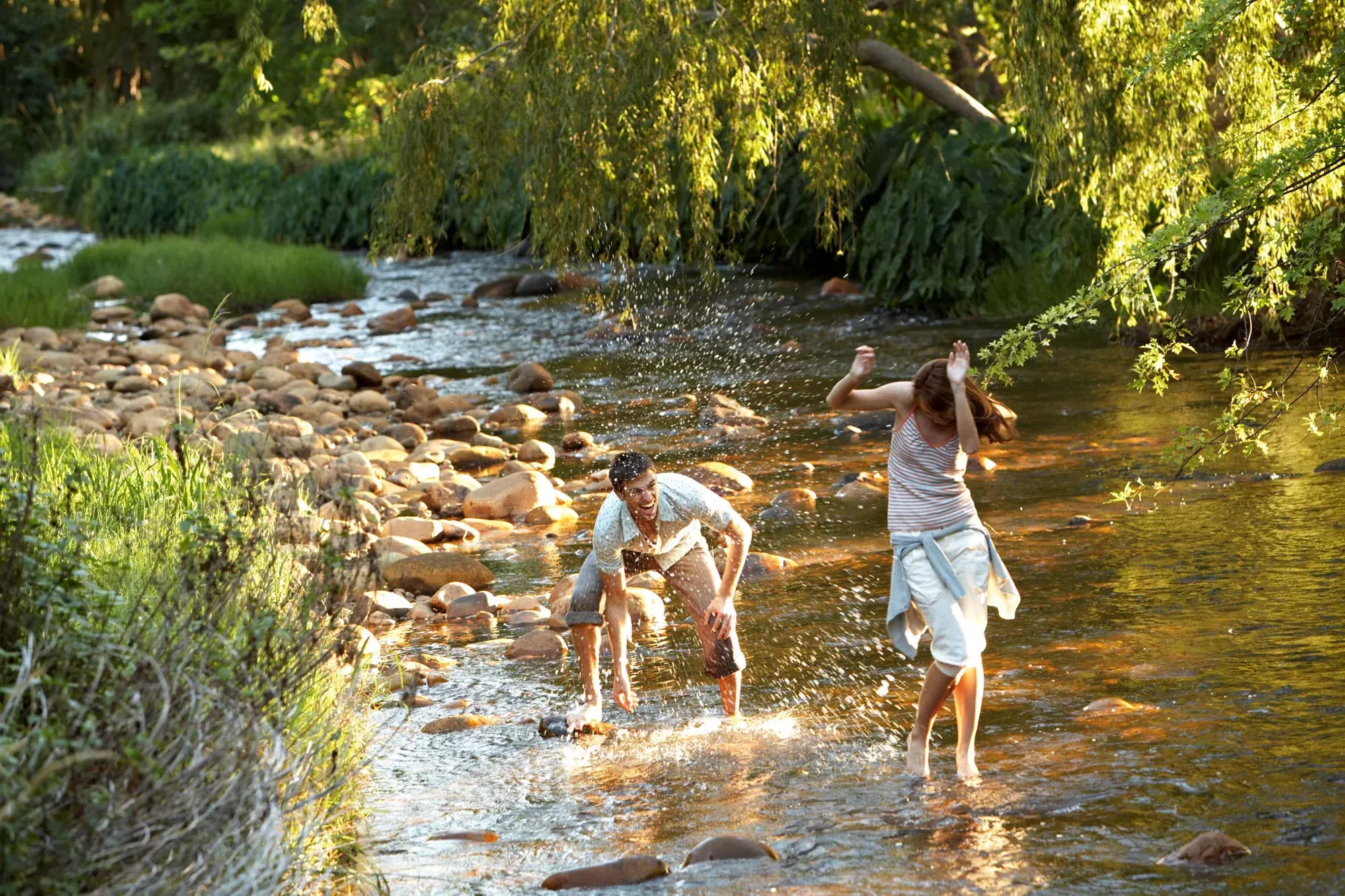 Junges Paar steht in Kleidern in einem Bach und bespritzt sich gegenseitig mit Wasser. Junges Paar steht in Kleidern in einem Bach und bespritzt sich gegenseitig mit Wasser.