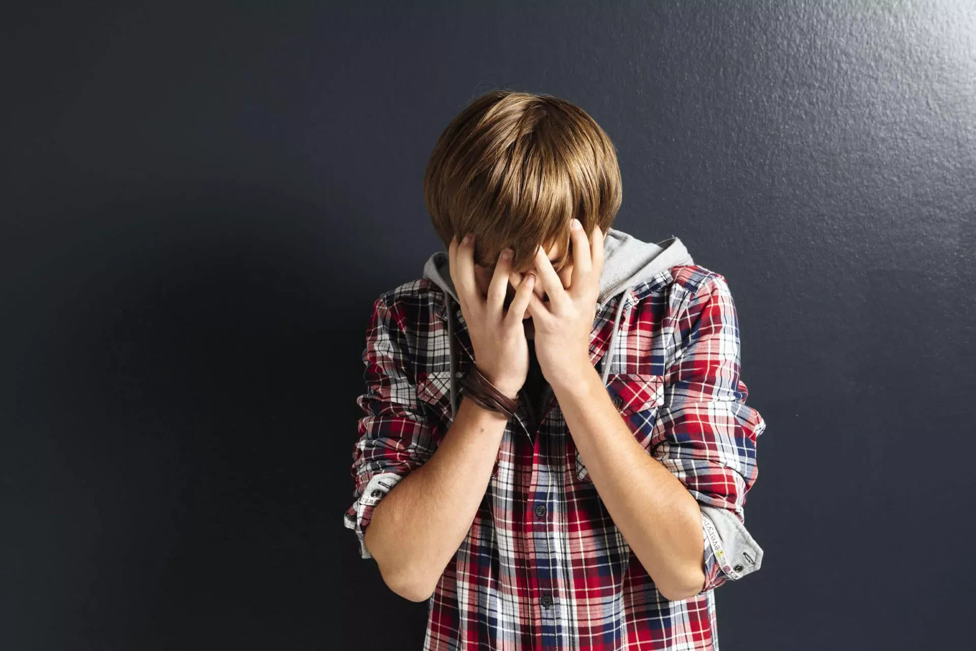 Deprimierter Teenager in kariertem Hemd mit den Händen vor dem Gesicht. Deprimierter Teenager in kariertem Hemd mit den Händen vor dem Gesicht.