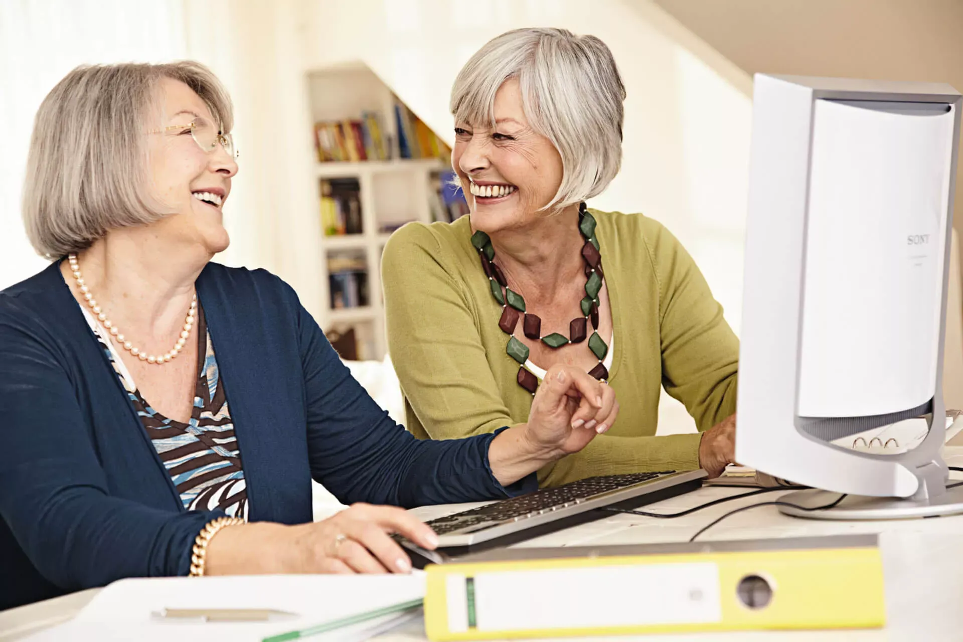 Zwei Seniorinnen sitzen gemeinsam am Computer und lachen sich an. Zwei Seniorinnen sitzen gemeinsam am Computer und lachen sich an.