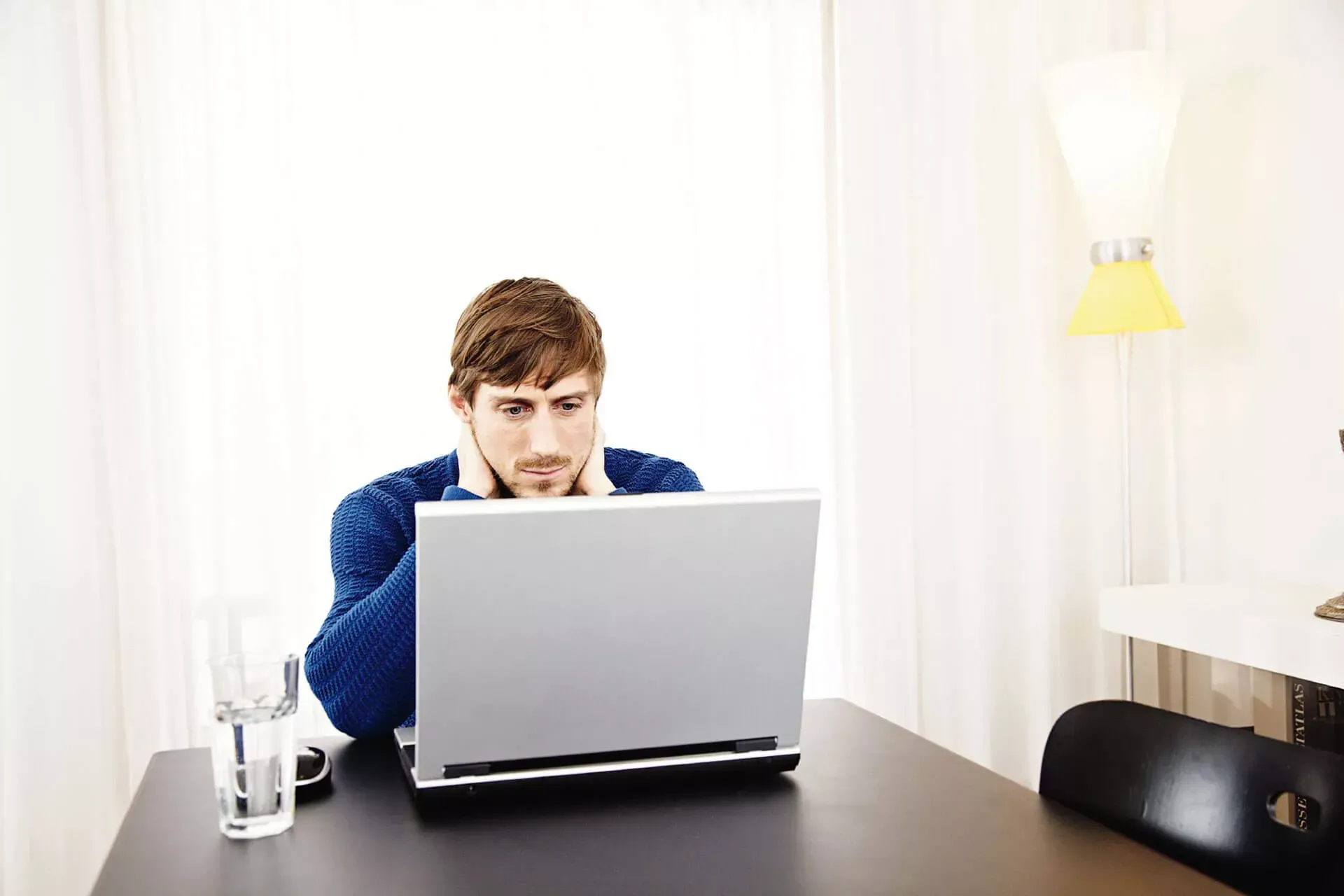 Junger Mann sitzt zuhause an seinem Notebook mit einem Glas Wasser daneben. Junger Mann sitzt zuhause an seinem Notebook mit einem Glas Wasser daneben.
