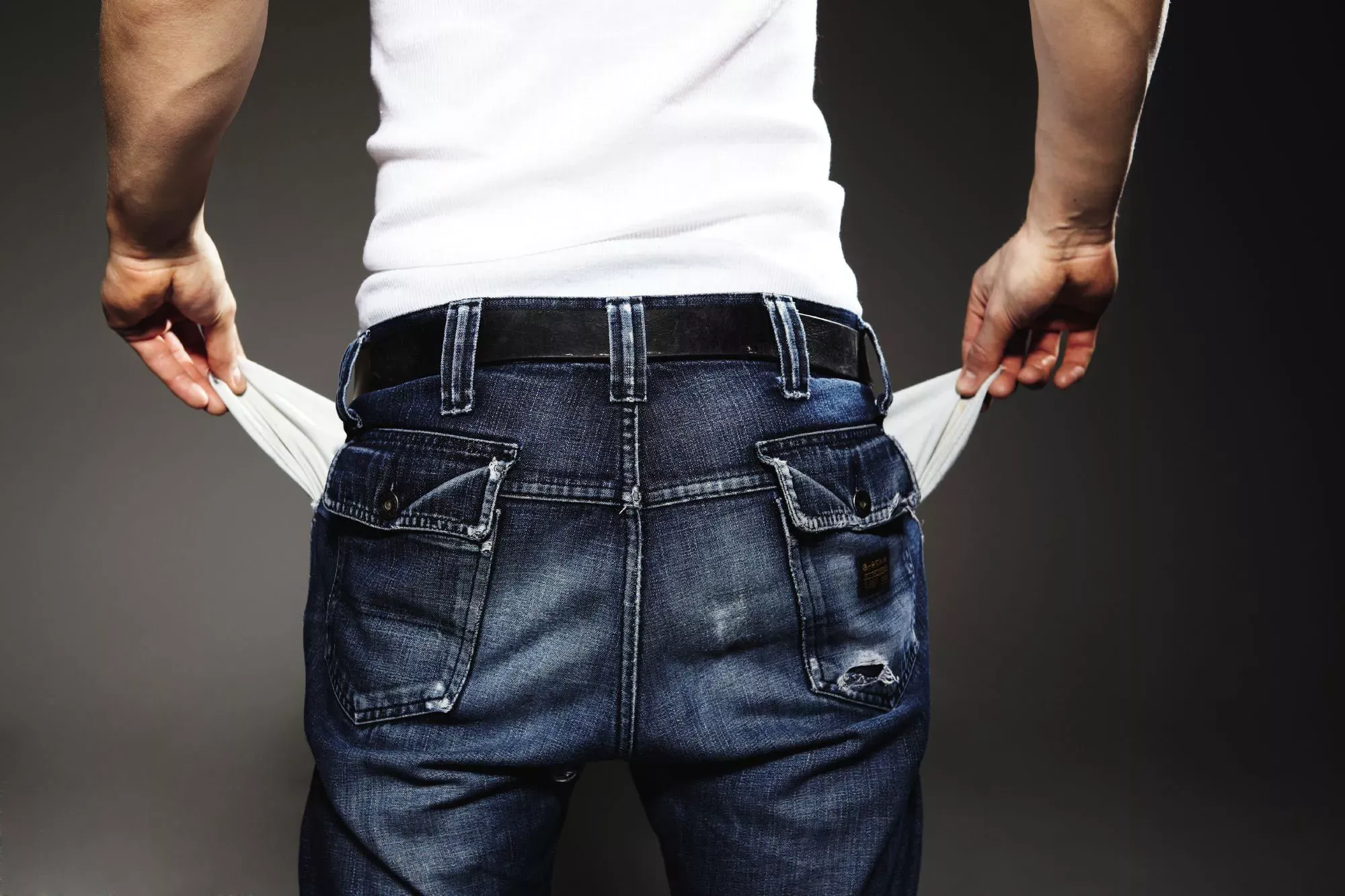 Rückansicht eines Mannes in weißem T-Shirt und Jeanshose, der seine leeren Hosentaschen zeigt. Rückansicht eines Mannes in weißem T-Shirt und Jeanshose, der seine leeren Hosentaschen zeigt.