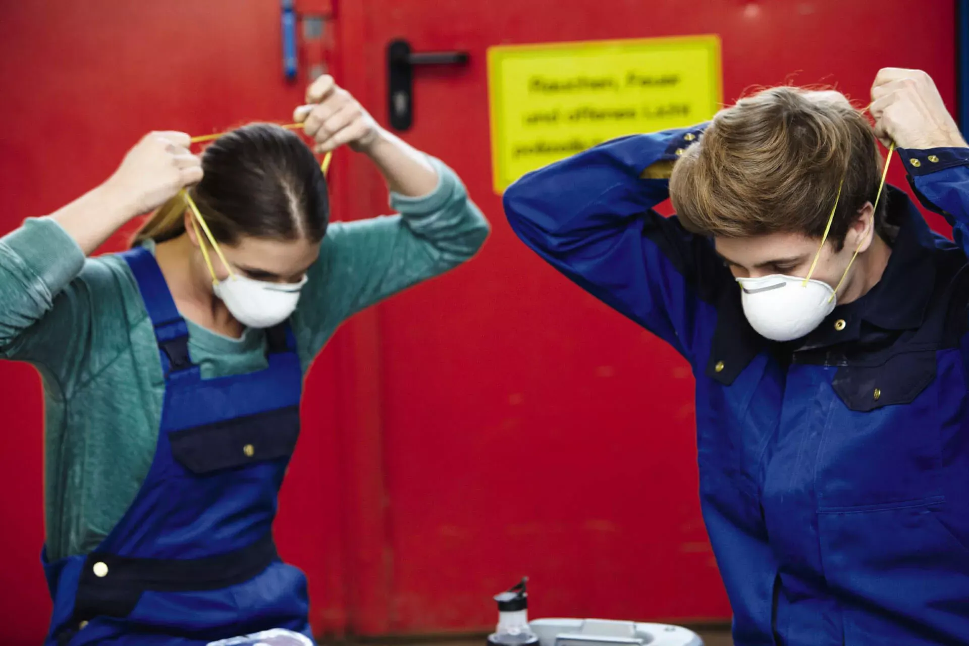Zwei Auszubildende im Handwerk ziehen sich Atemschutzmasken an. Zwei Auszubildende im Handwerk ziehen sich Atemschutzmasken an.