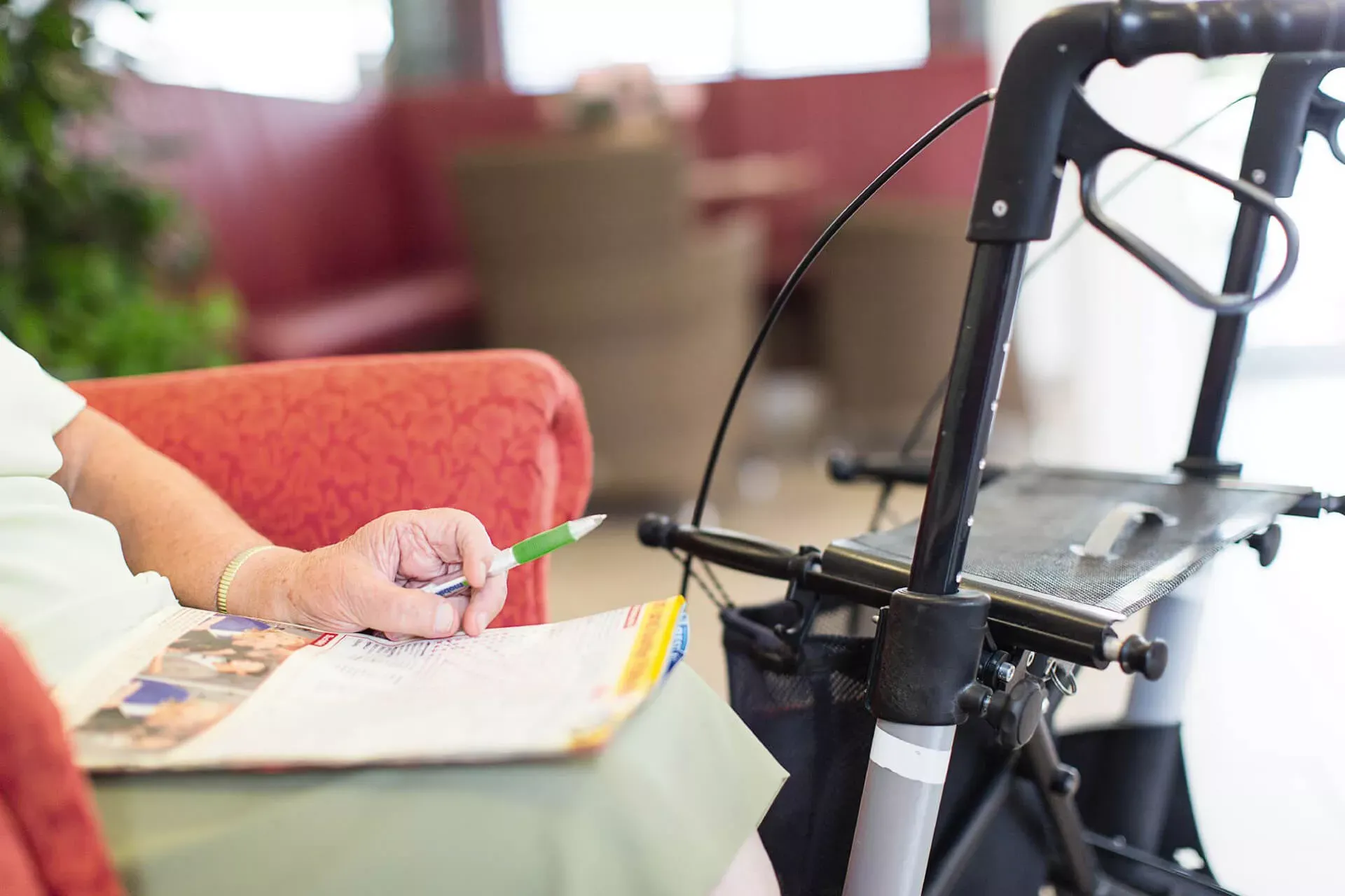 Seniorina sitzt neben ihrem Rollator auf einem Sessel mit einem Stift in der Hand und einem Kreuzworträtsel auf dem Schoß. Seniorina sitzt neben ihrem Rollator auf einem Sessel mit einem Stift in der Hand und einem Kreuzworträtsel auf dem Schoß.