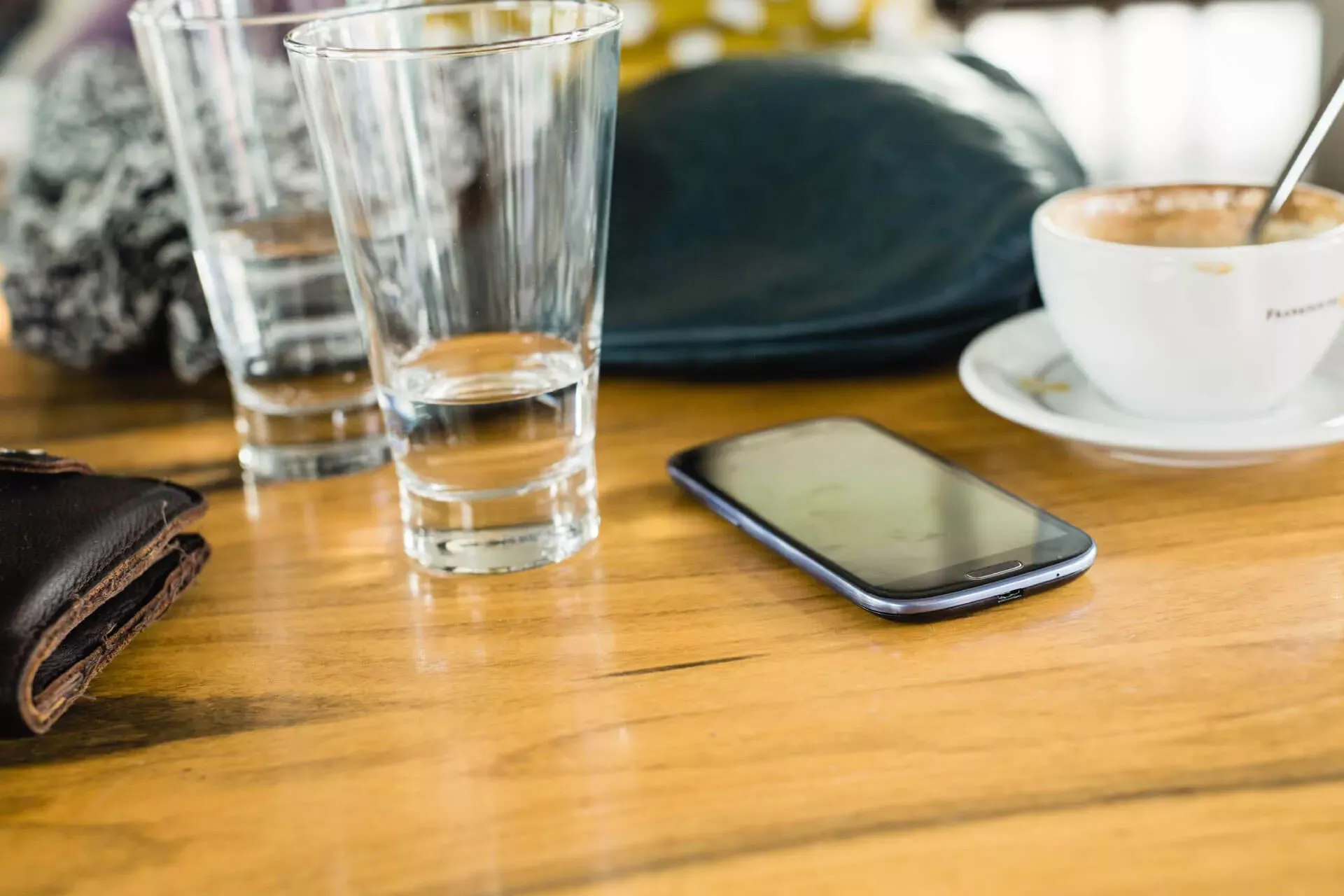 Smartphone liegt auf einem Restauranttisch neben Tassen, Gläsern und einem Geldbeutel. Smartphone liegt auf einem Restauranttisch neben Tassen, Gläsern und einem Geldbeutel.