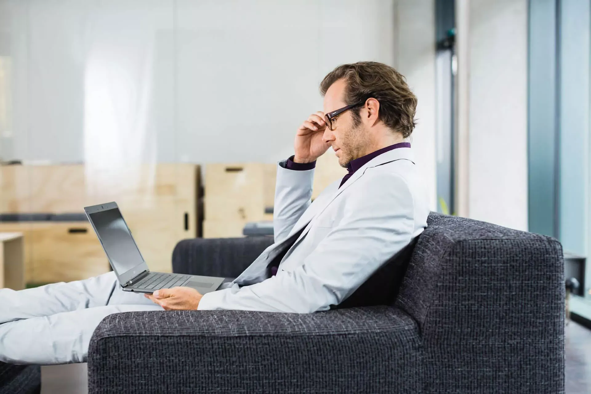 Mann sitzt im Anzug auf einem Sofa mit Notebook, im Hintergrund Umzugskisten. Mann sitzt im Anzug auf einem Sofa mit Notebook, im Hintergrund Umzugskisten.