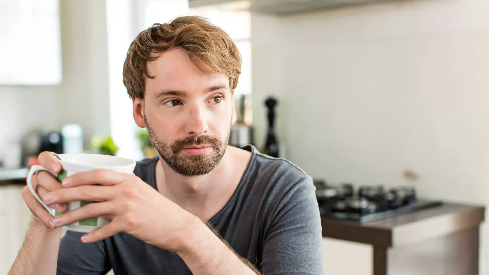 Junger Mann sitzt in der Küche und hält eine Tasse mit beiden Händen. – Bildnachweis: wdv.de © J.Lauer Junger Mann sitzt in der Küche und hält eine Tasse mit beiden Händen. – Bildnachweis: wdv.de © J.Lauer