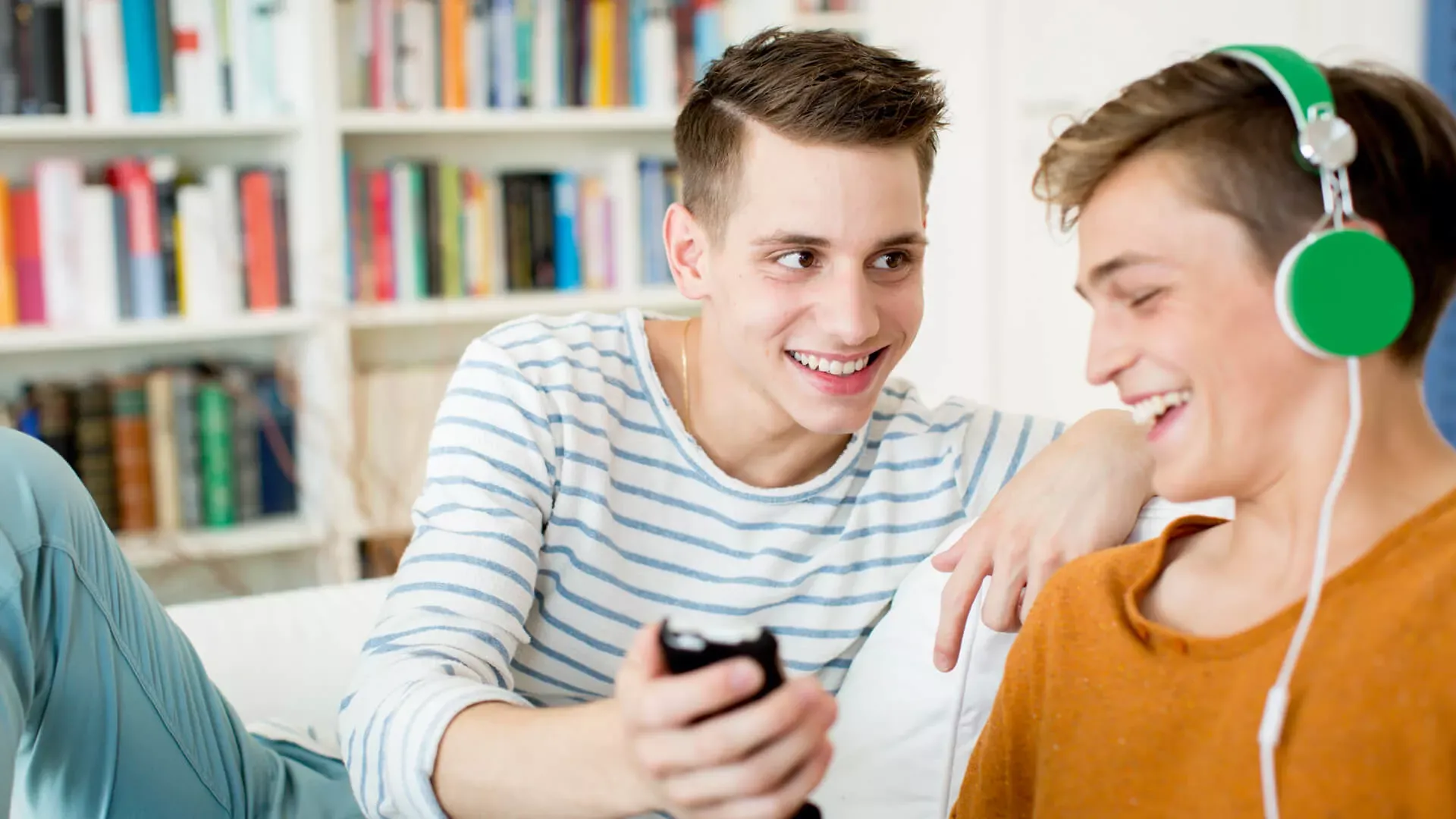 Zwei Jungs im Teenageralter sitzen auf dem Sofa im Wohnzimmer und schauen lachend in ein Smartphone. – Bildnachweis: wdv.de © Szekely.Oana Zwei Jungs im Teenageralter sitzen auf dem Sofa im Wohnzimmer und schauen lachend in ein Smartphone. – Bildnachweis: wdv.de © Szekely.Oana