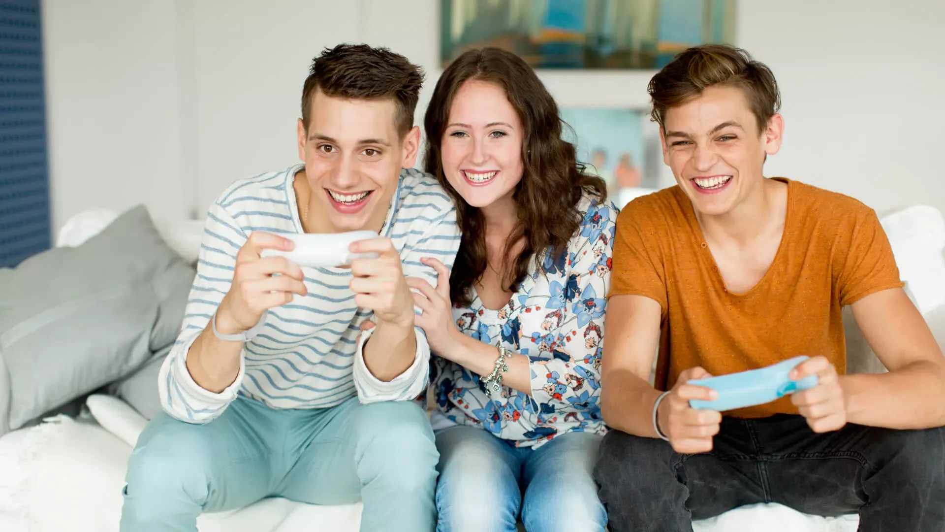 Zwei Jungen und ein Mädchen im Teenageralter sitzen auf dem Sofa und zocken mit Fernbedienungen einer Spielkonsole. – Bildnachweis: wdv.de © Szekely.Oana Zwei Jungen und ein Mädchen im Teenageralter sitzen auf dem Sofa und zocken mit Fernbedienungen einer Spielkonsole. – Bildnachweis: wdv.de © Szekely.Oana