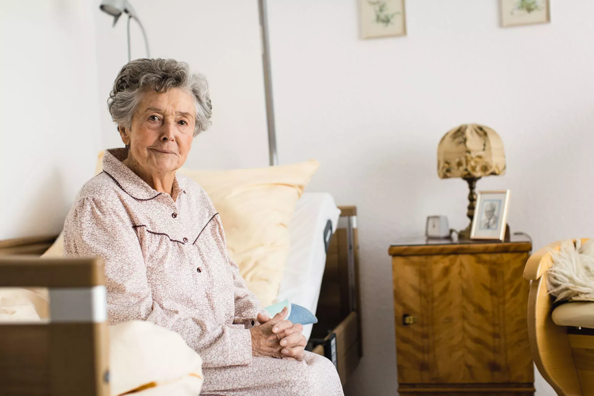 Seniorin sitzt im Nachthemd auf der Bettkante in ihrem Pflegeheimzimmer. Seniorin sitzt im Nachthemd auf der Bettkante in ihrem Pflegeheimzimmer.
