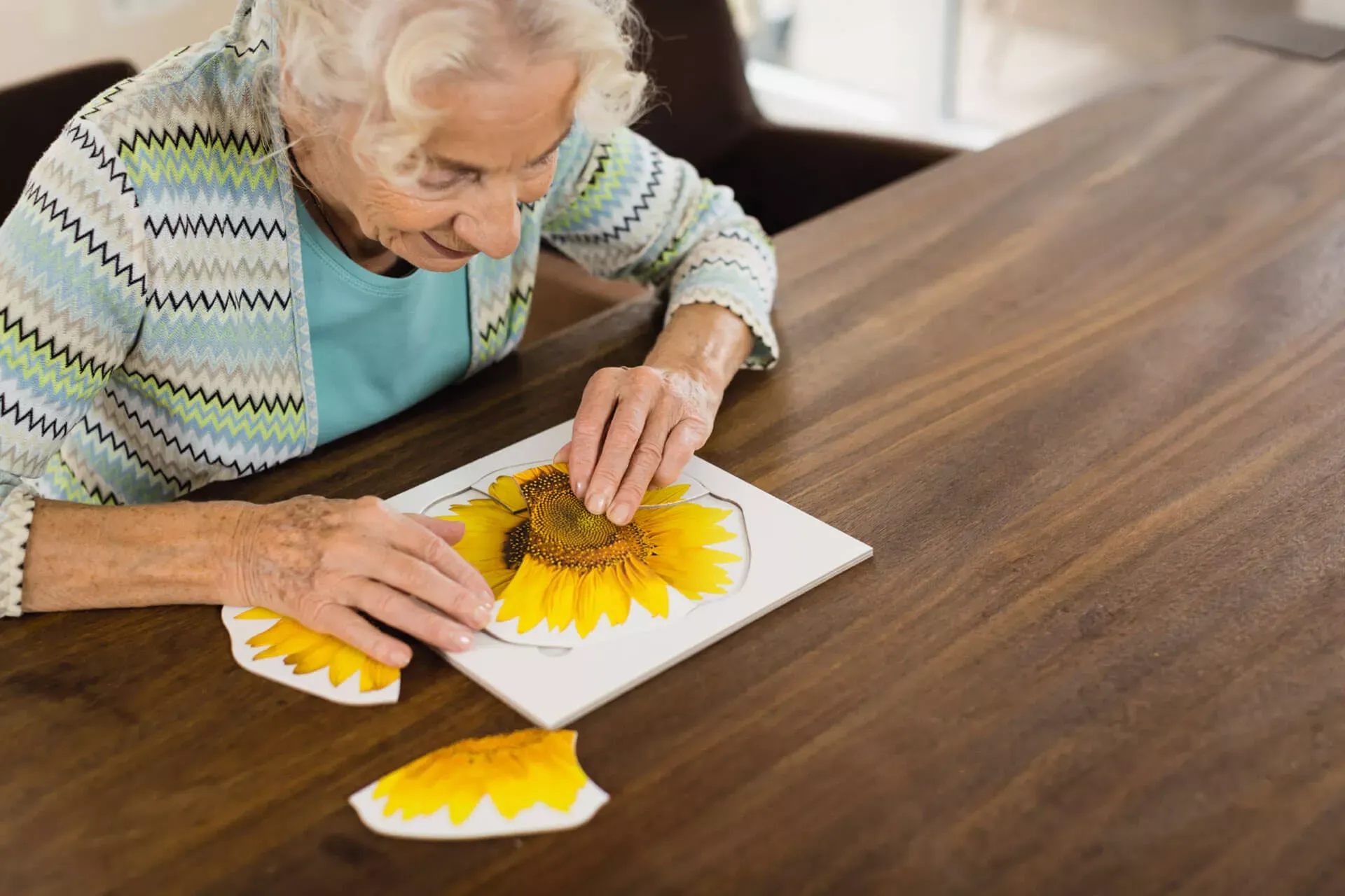Seniorin sitzt an einem Tisch und macht ein Blumenpuzzle als geistige Übung und Demenzprophylaxe. Seniorin sitzt an einem Tisch und macht ein Blumenpuzzle als geistige Übung und Demenzprophylaxe.