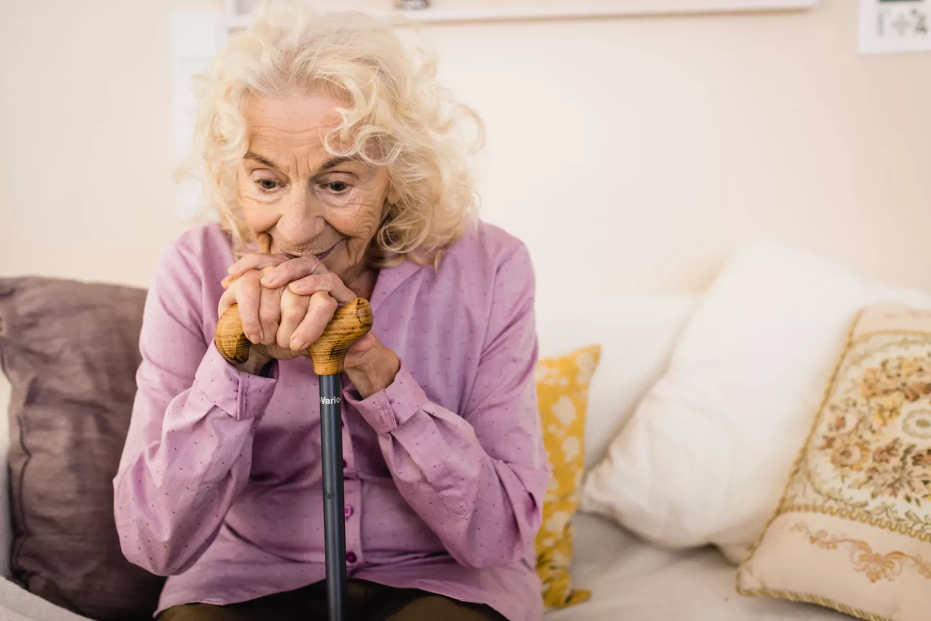Seniorin sitzt auf ihrem Sofa und stützt die Hände auf einen Gehstock. Seniorin sitzt auf ihrem Sofa und stützt die Hände auf einen Gehstock.