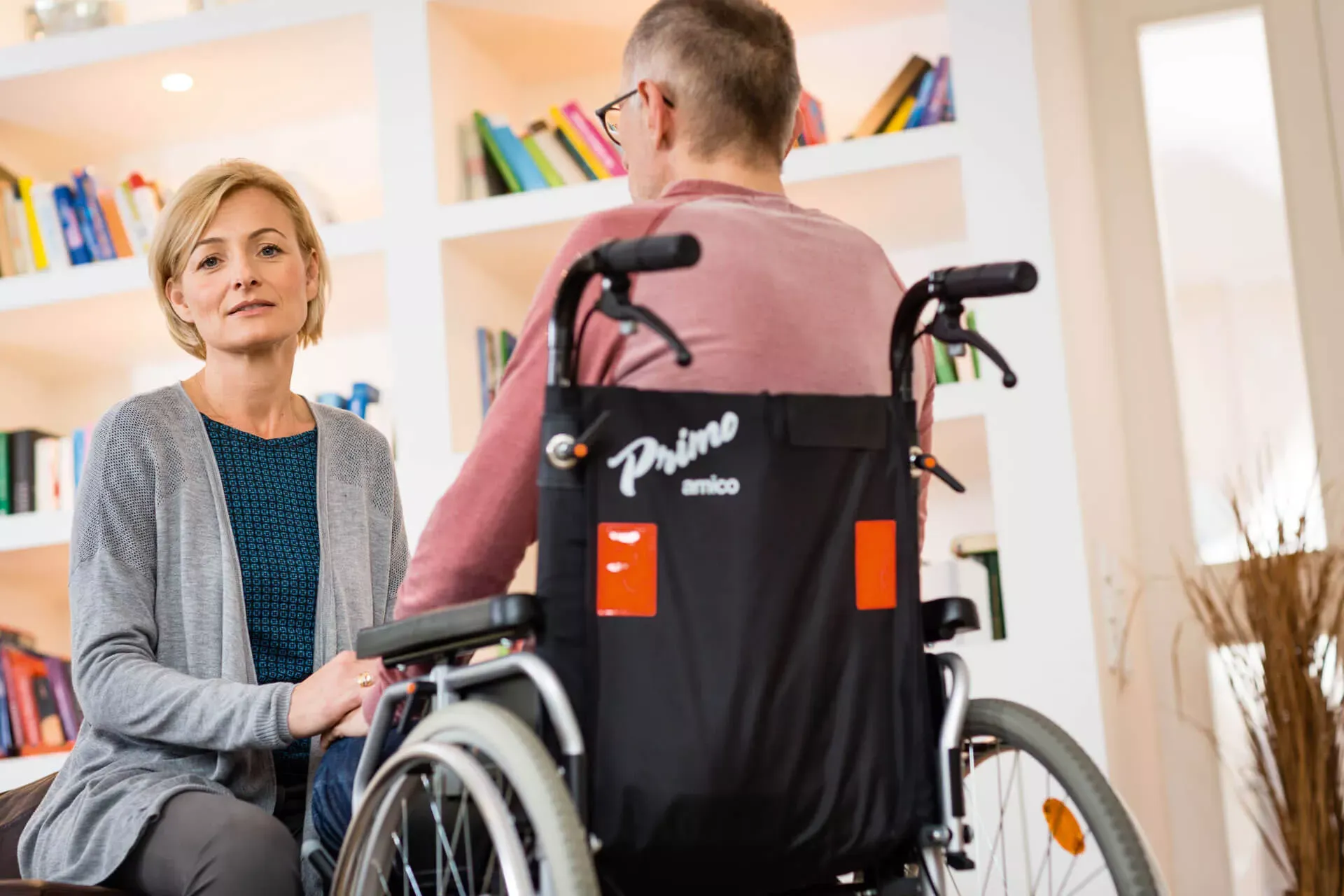 Frau sitzt vor einem Mann mit Behinderung im Rollstuhl und schaut in die Kamera. Frau sitzt vor einem Mann mit Behinderung im Rollstuhl und schaut in die Kamera.