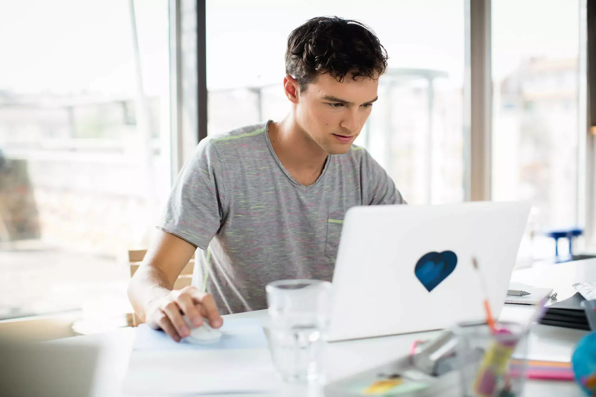 Junger Mann sitzt zuhause am Notebook mit einem Glas Wasser auf dem Tisch. Junger Mann sitzt zuhause am Notebook mit einem Glas Wasser auf dem Tisch.
